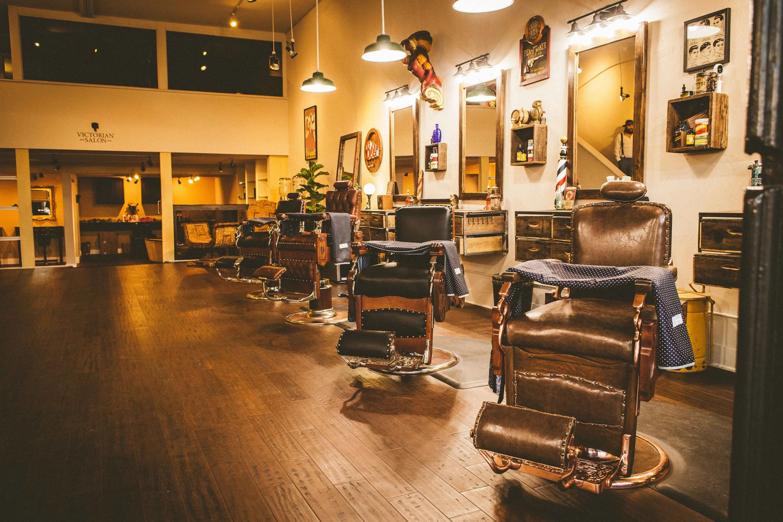 Interior of a vintage-style barbershop with old-fashioned barber chairs and mirrors, warm lighting, and decorative wall art.