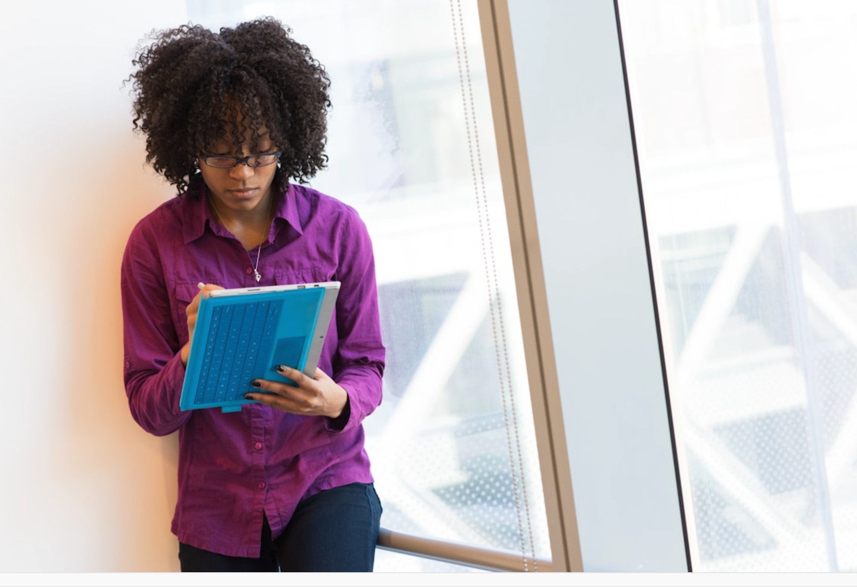 A young Black woman with a holding a tablet with a keyboard attachment typing. The overall mood is focused and contemplative, suggesting a moment of work and study.