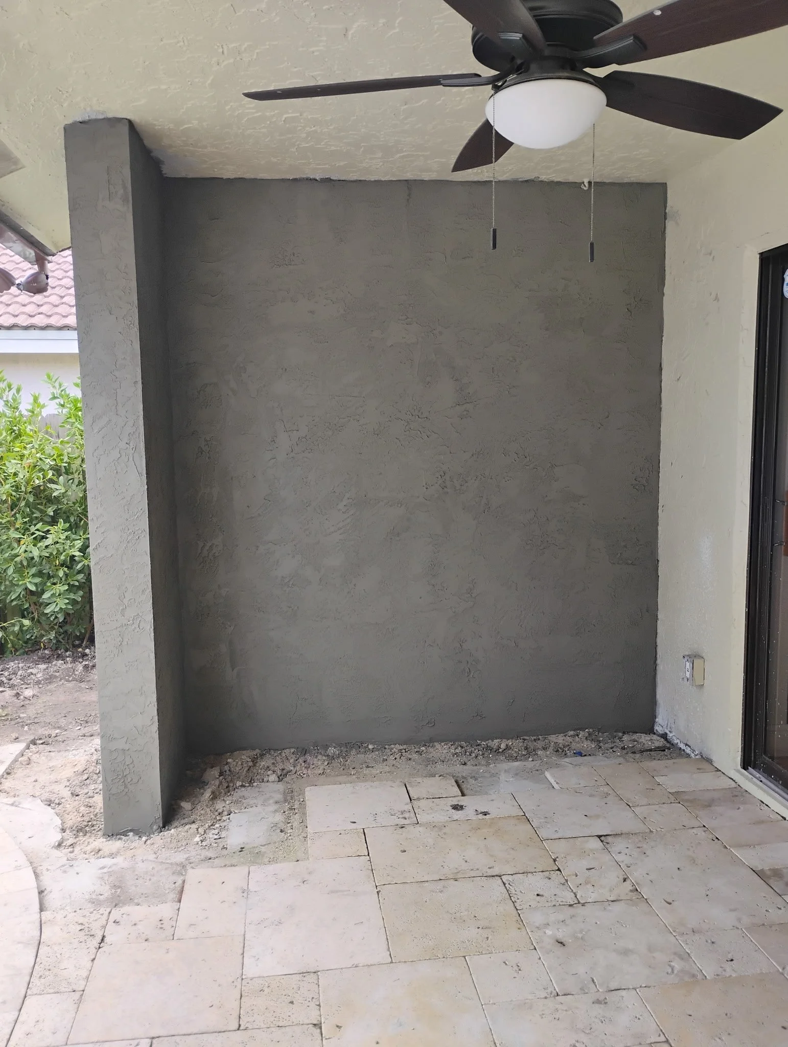 Patio with a newly stocco gray wall, unfinished flooring, and a ceiling fan with a light. 