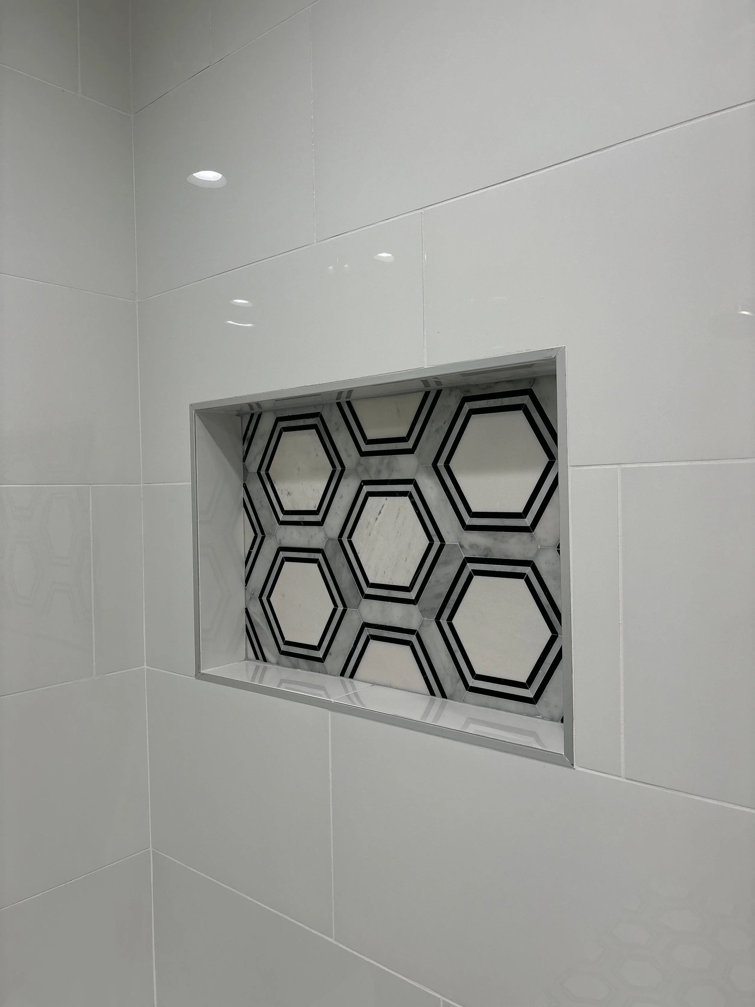 A built-in shower niche with hexagonal black and white patterned tiles, surrounded by white tiled walls.