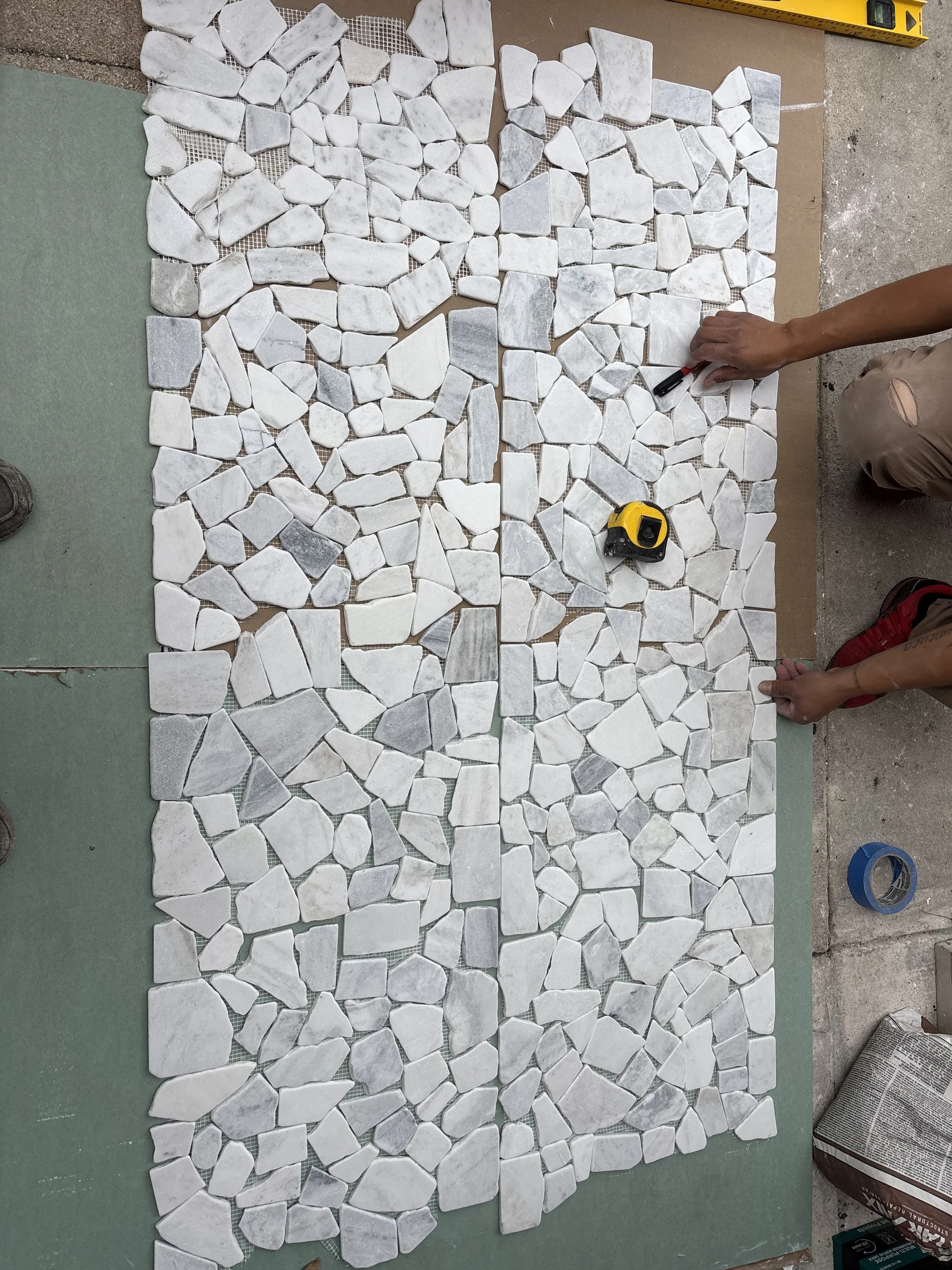 Our tiling expert working on laying out white marble mosaic tiles on a floor for a tiling project.