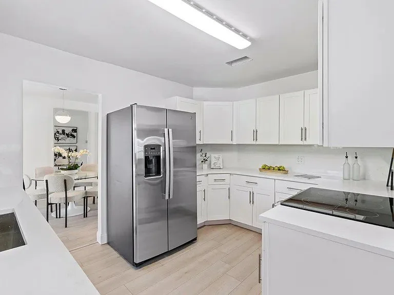 Clean, modern kitchen with white cabinets and stainless steel refrigerator in a bright room.