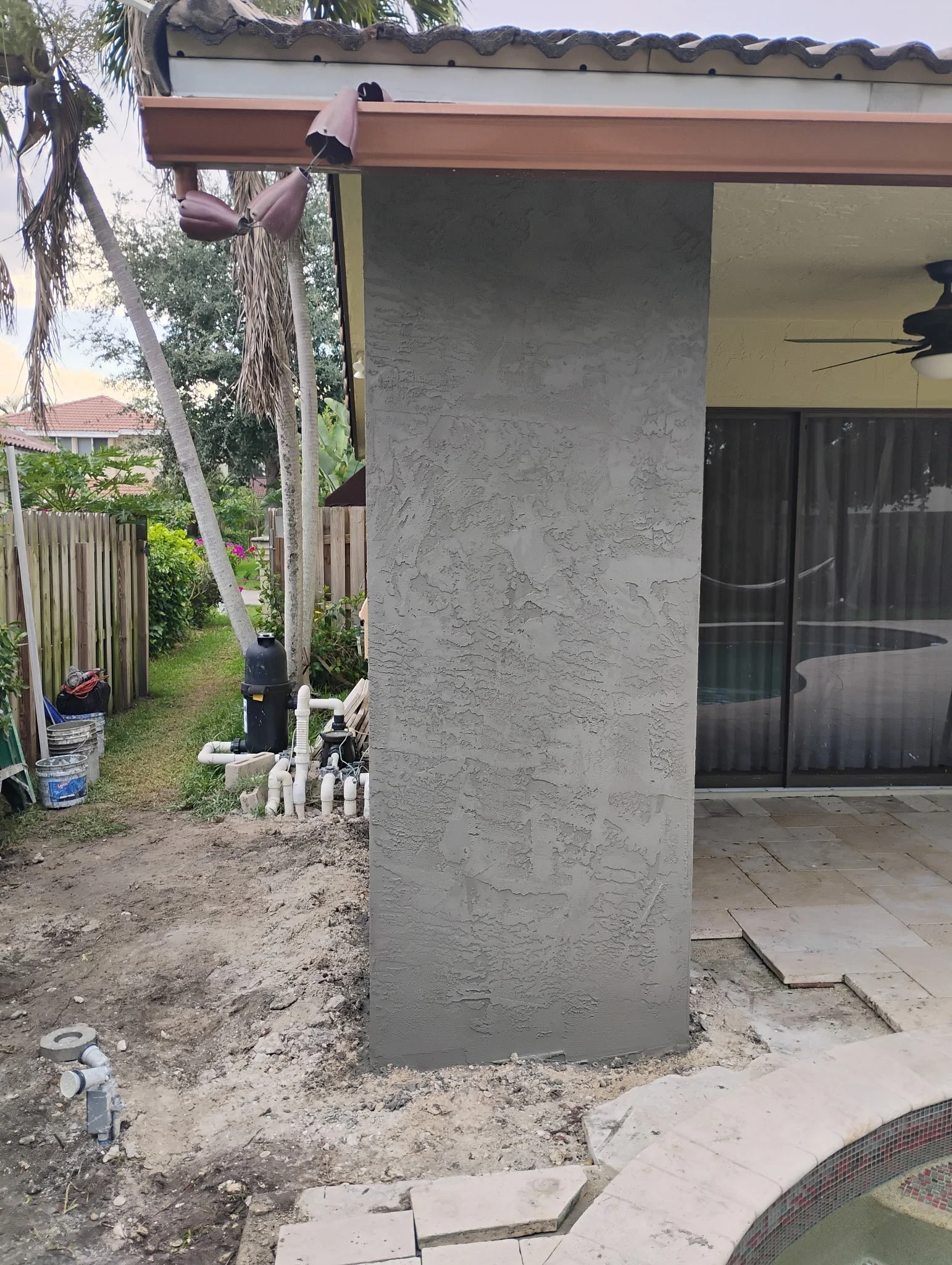 Side view of house corner with a textured stucco wall, construction work ongoing on the ground.