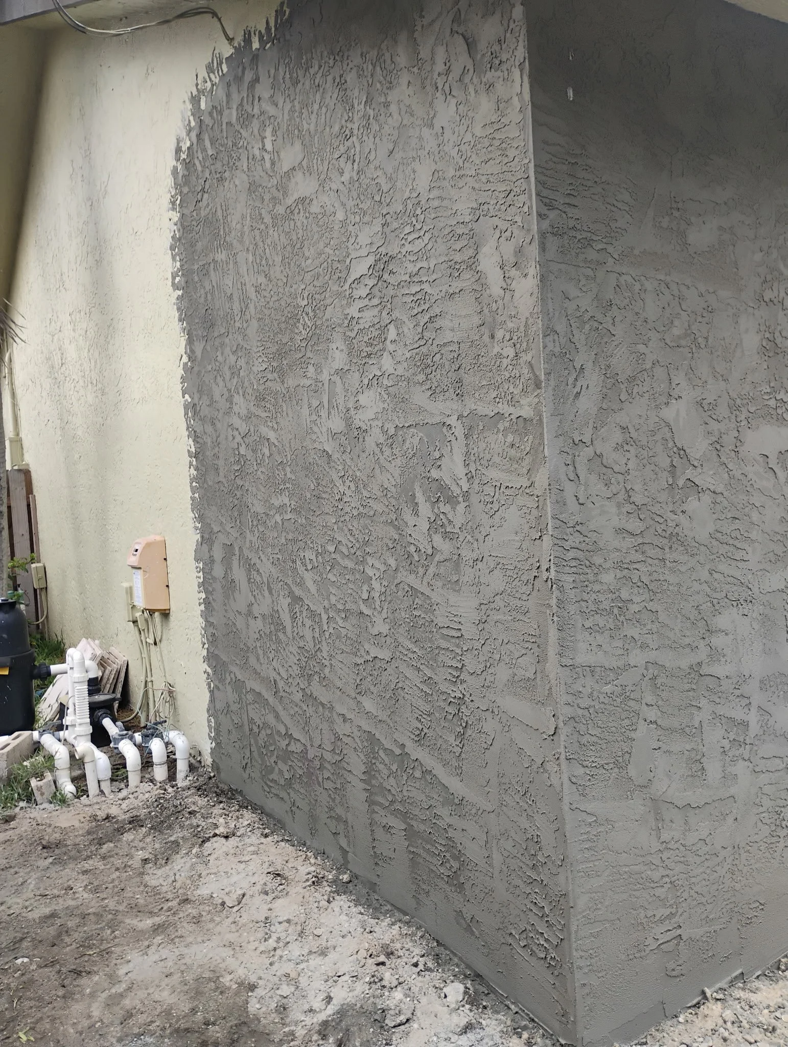 Gray textured exterior wall with finished stucco matching previous textured cream-colored wall 
