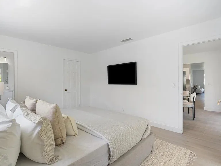 Minimalist bedroom with a bed, multiple pillows, white walls, a door, and a mounted flat-screen TV