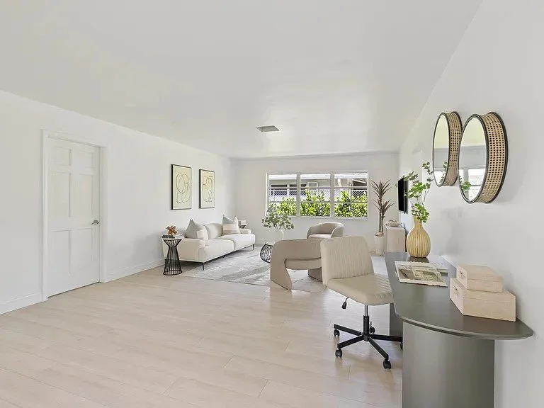 Minimalist living room with white walls, light-colored wooden floor, a white sofa, a beige armchair, a desk with a chair, potted plants, and round mirrors on the wall.