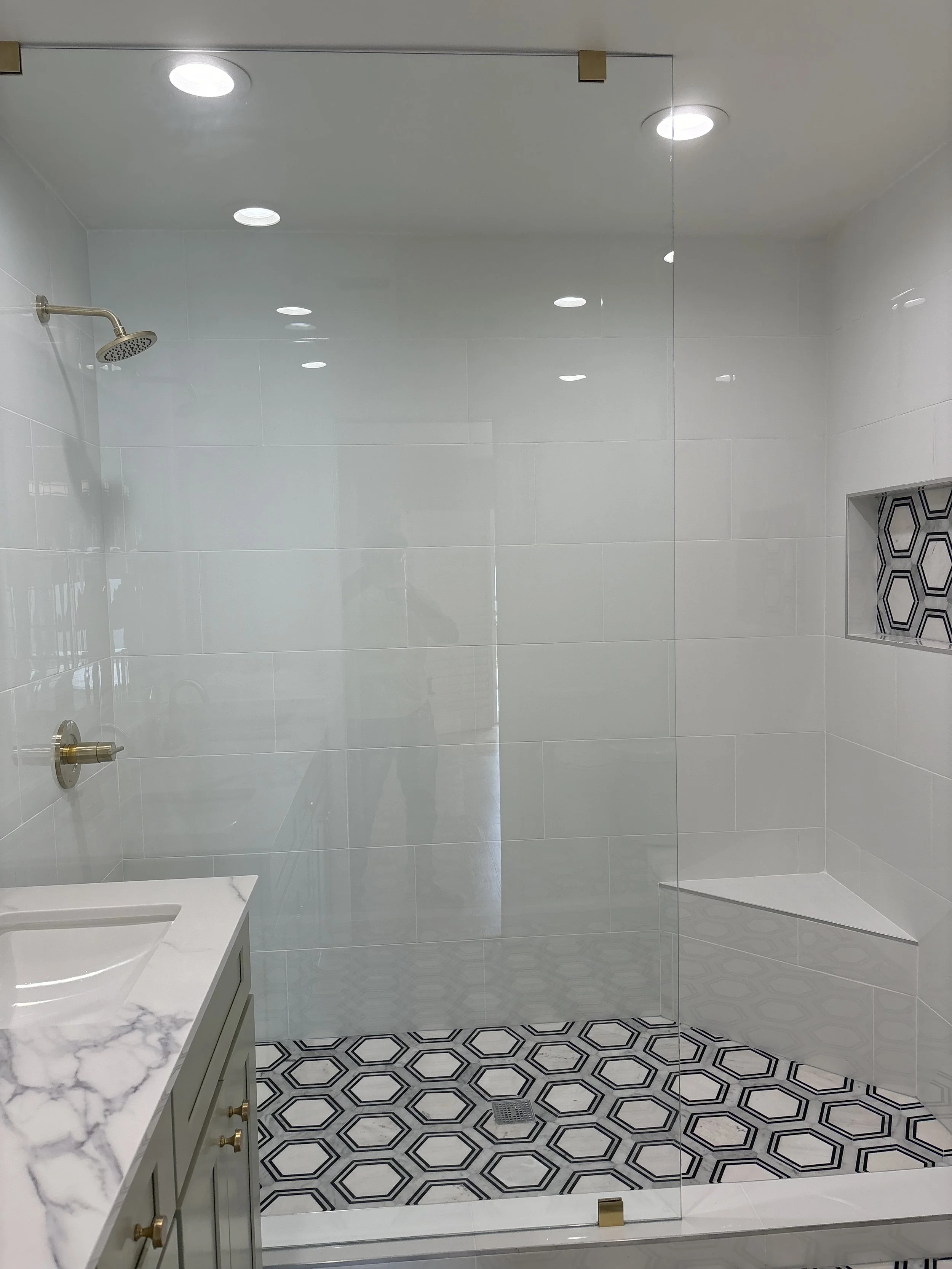 Modern walk-in shower with a glass door, hexagon patterned black and white tile floor, built-in shower shelf with hexagon tile, and a marble vanity countertop.