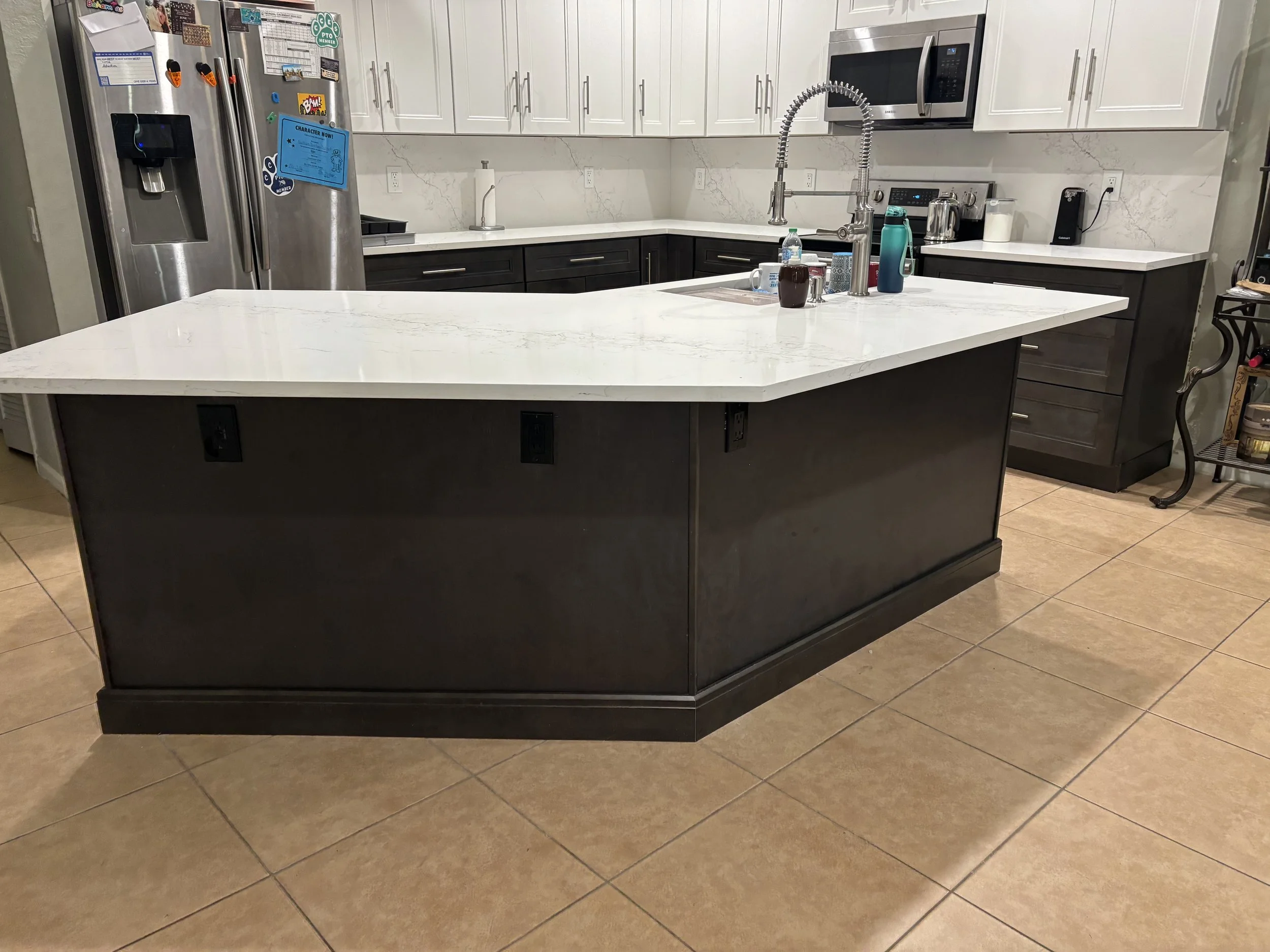 Modern kitchen with black and white cabinetry, a large island with a white Calcatta  countertop, stainless steel refrigerator, microwave, and various kitchen appliances.