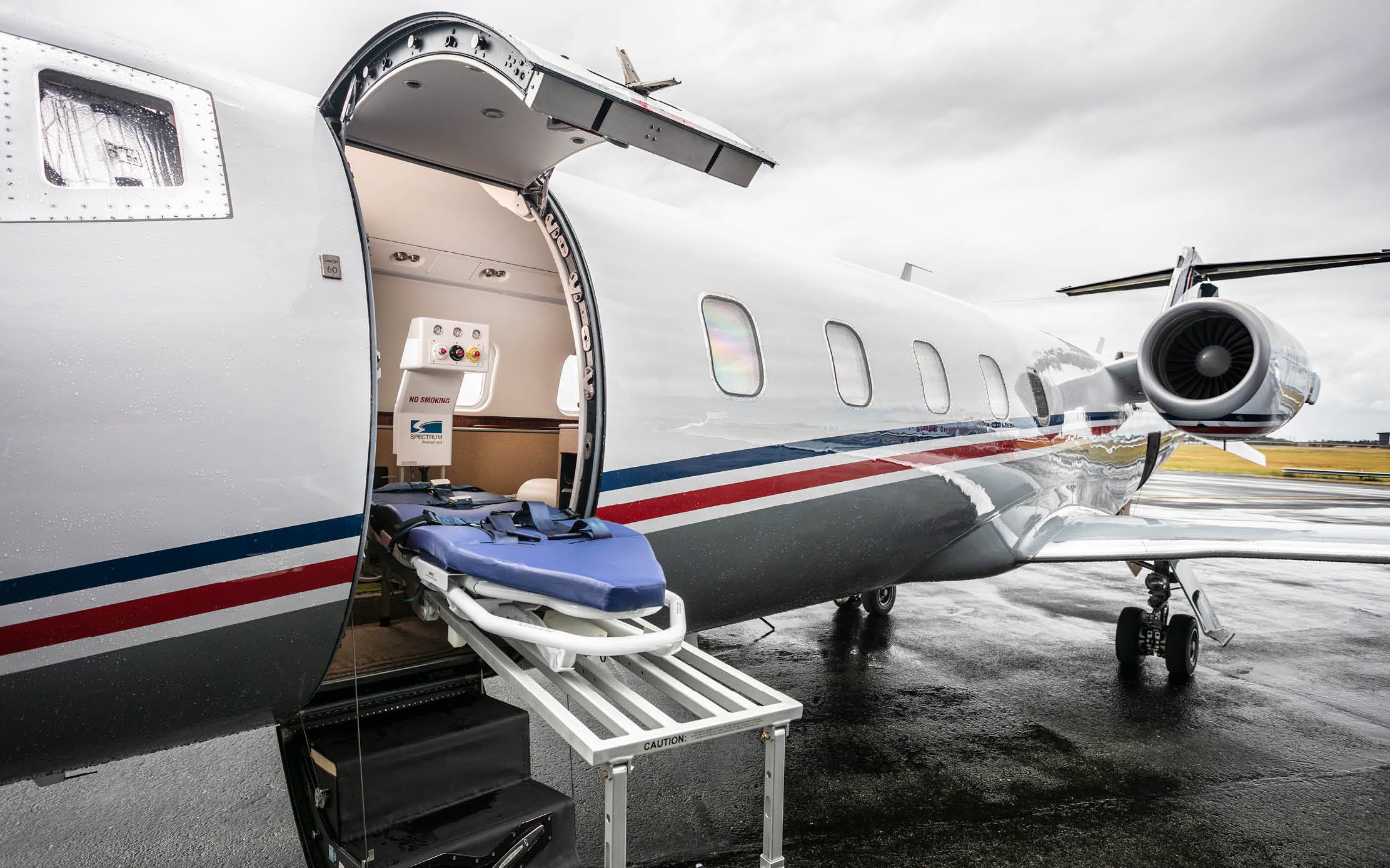 Private jet on tarmac with the door open, a stretcher positioned outside, and cloudy sky overhead.
