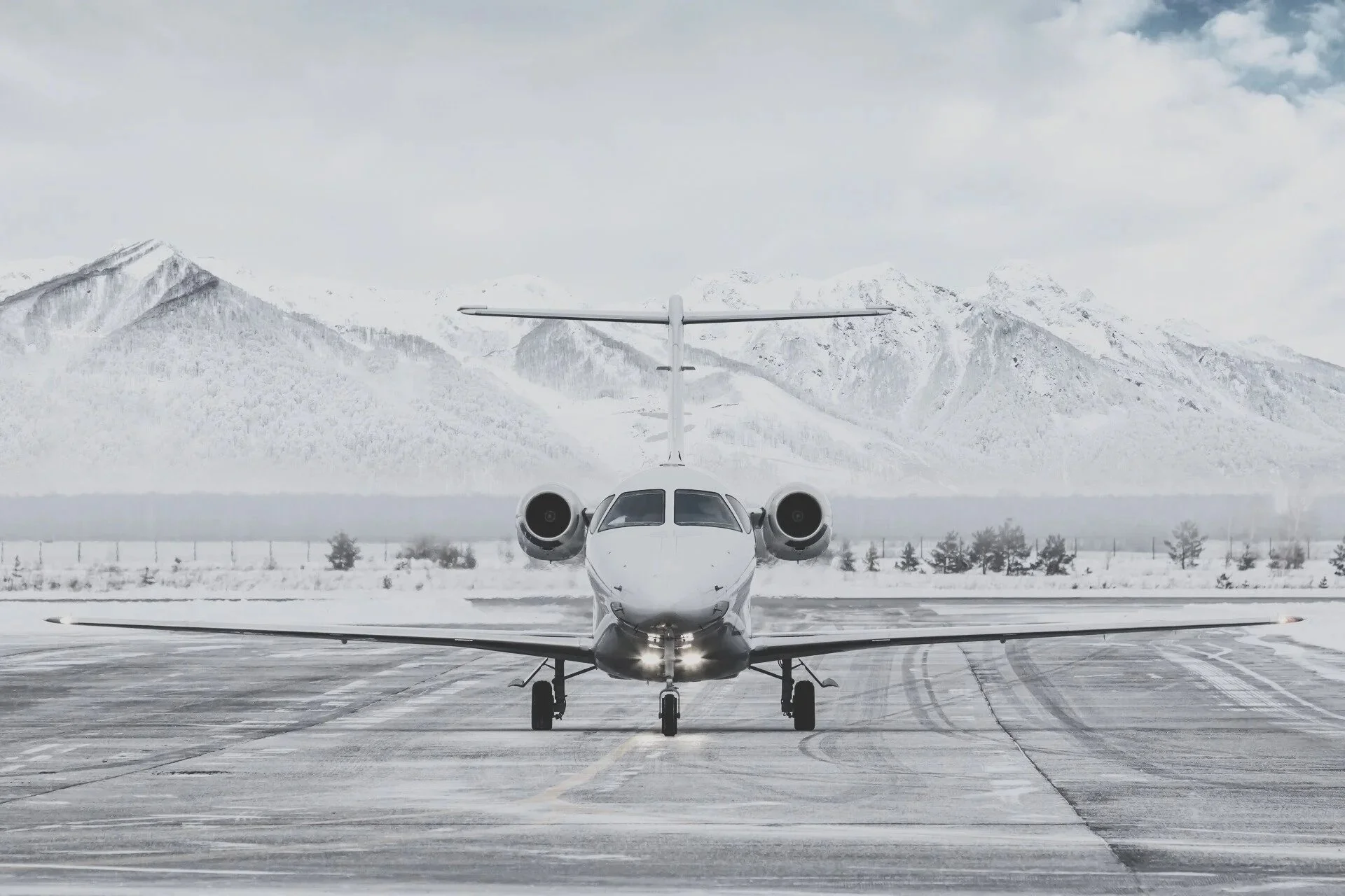 A private jet parked on an icy runway with snow-covered mountains in the background.