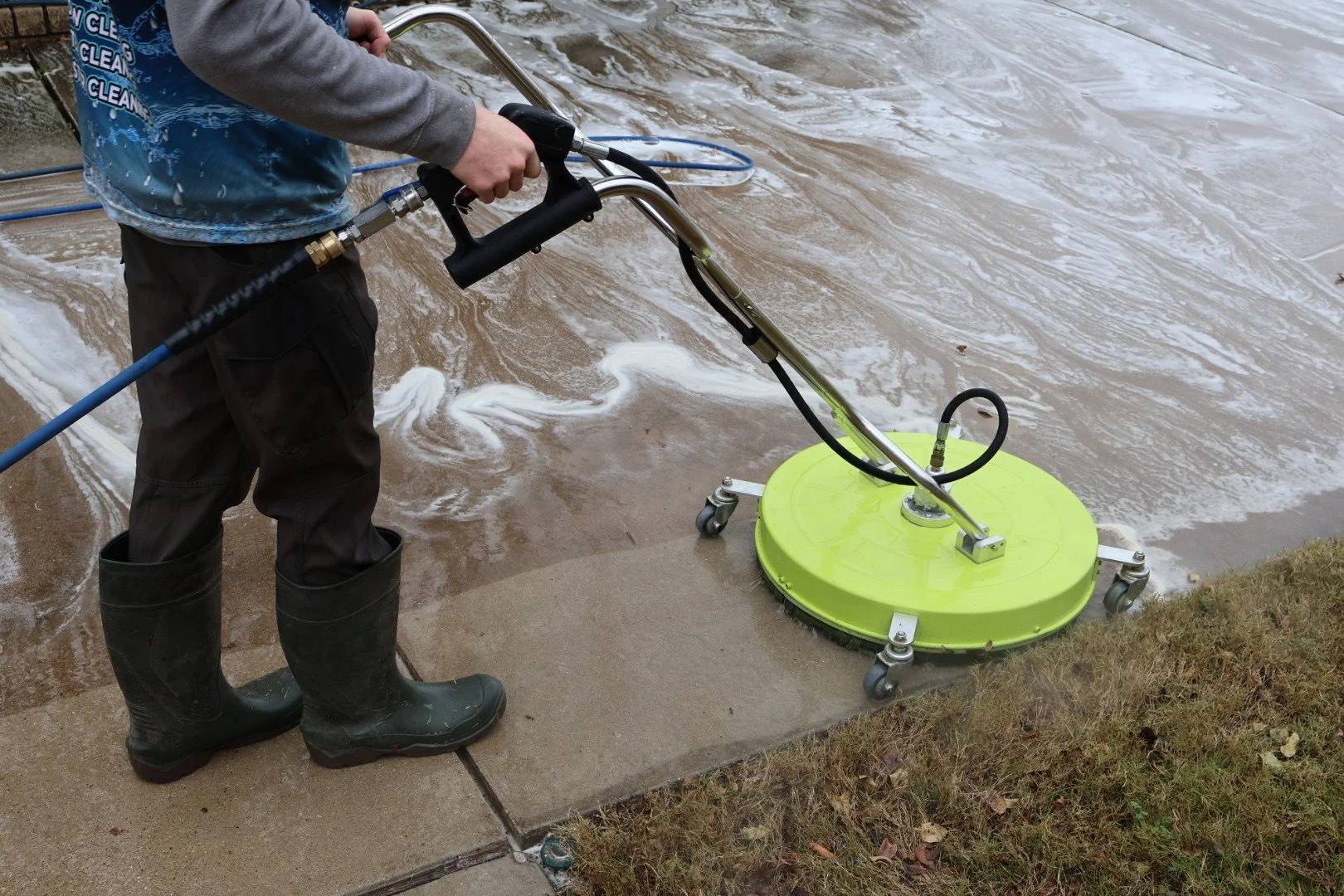 Person using a surface cleaner to wash a concrete sidewalk near water.