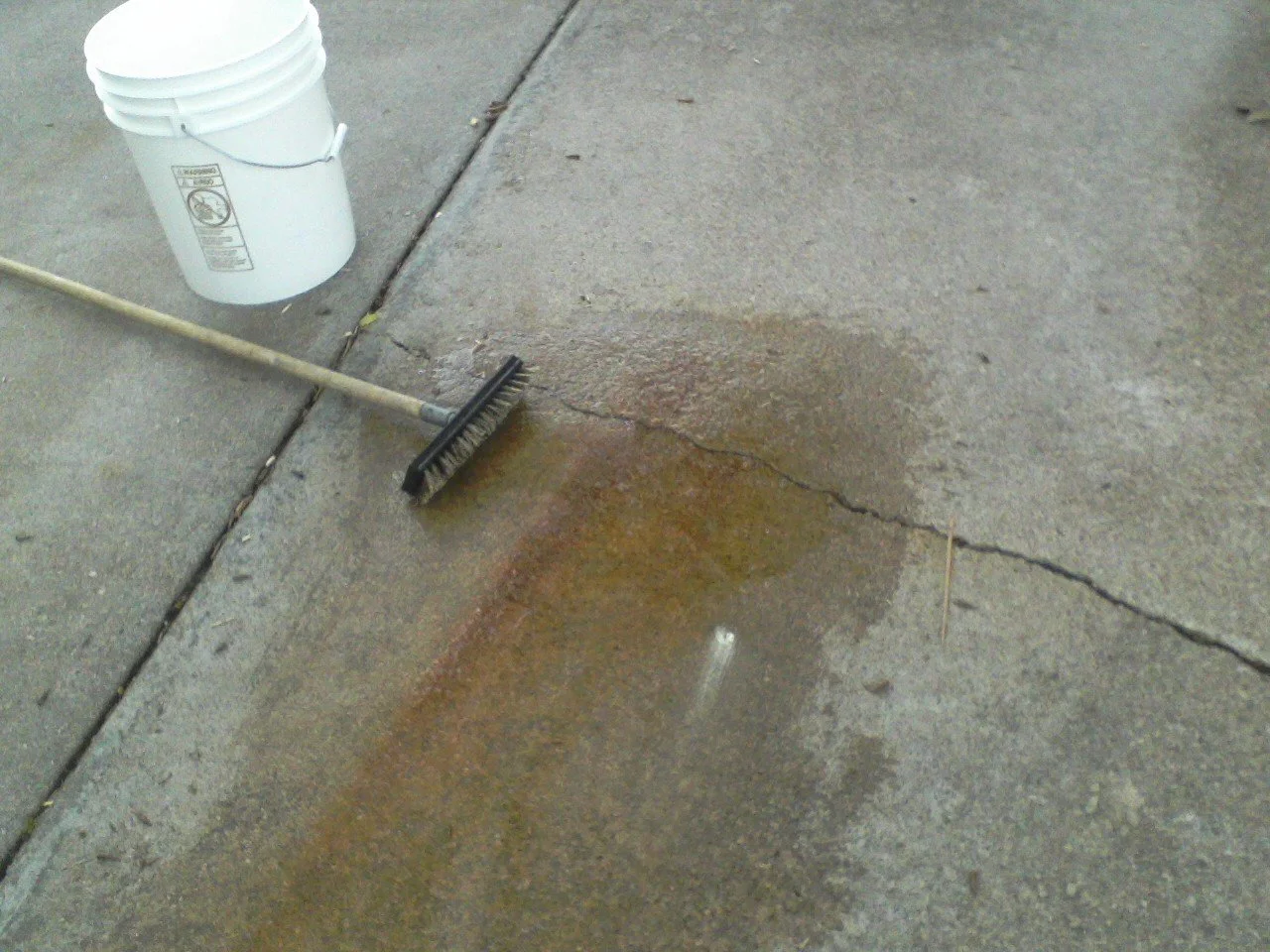 A sidewalk with a broom, a bucket, and a puddle of water
