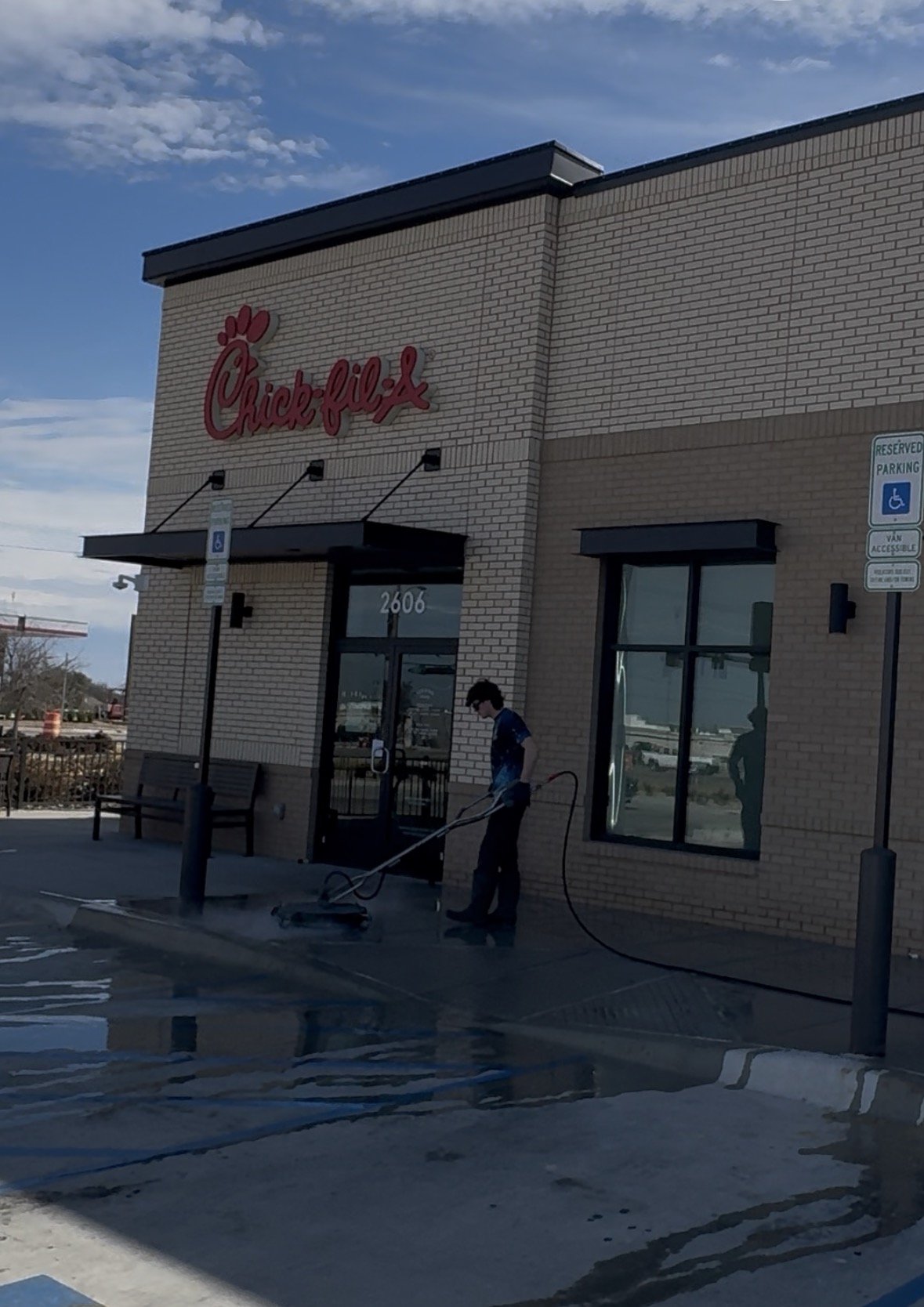 A person cleaning the parking lot outside a Chick-fil-A restaurant on a sunny day.