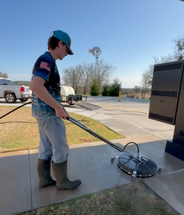 Boy in boots and cap using a pressure washer outside on a sunny day