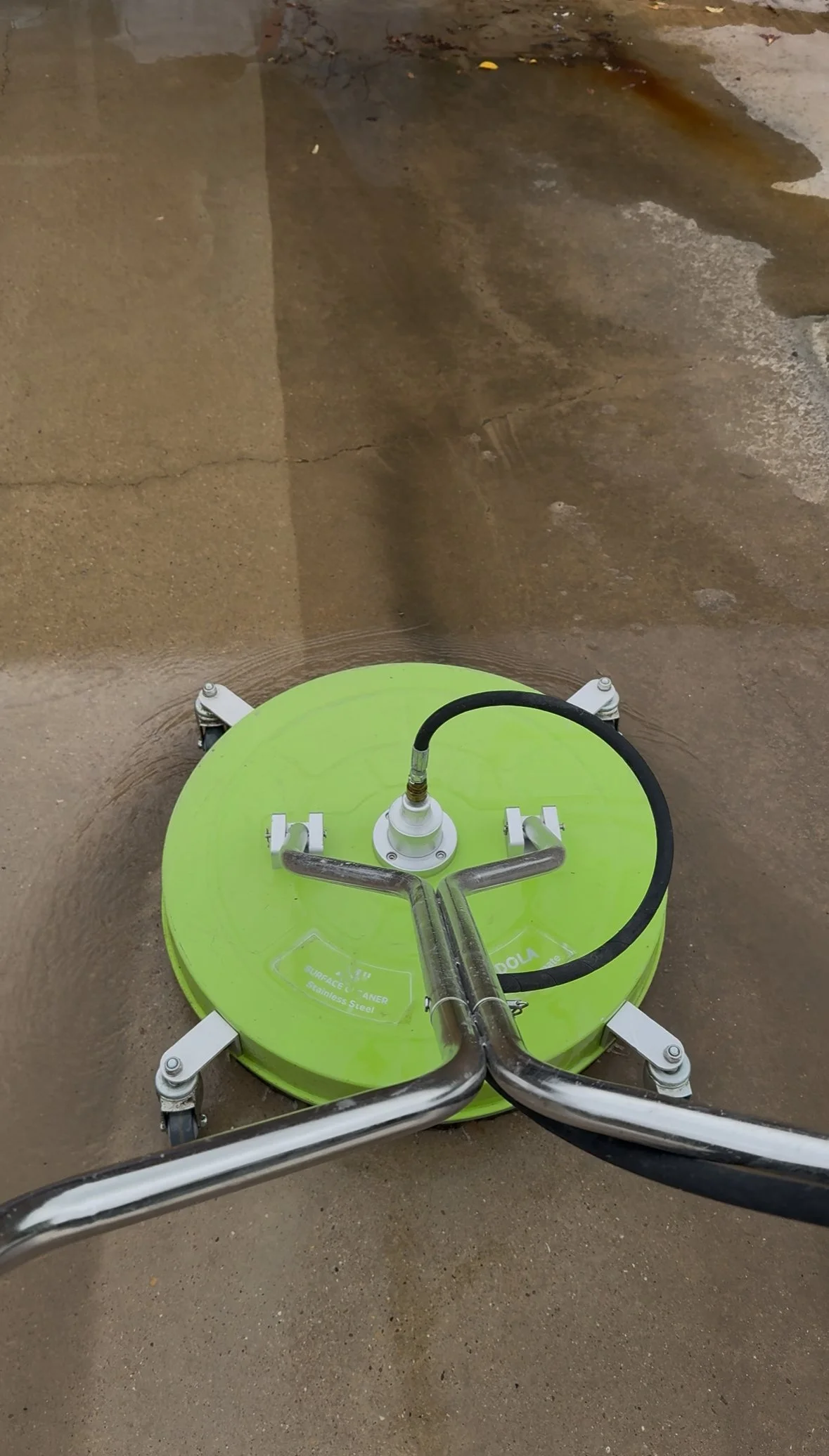 A floor cleaning machine with a bright green circular base moving over a concrete or stone floor, creating a wet path.