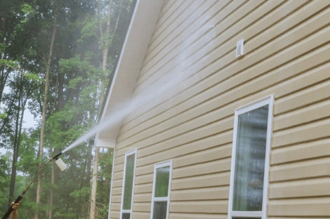 Power washer cleaning the beige vinyl siding of a house while spraying water upwards.