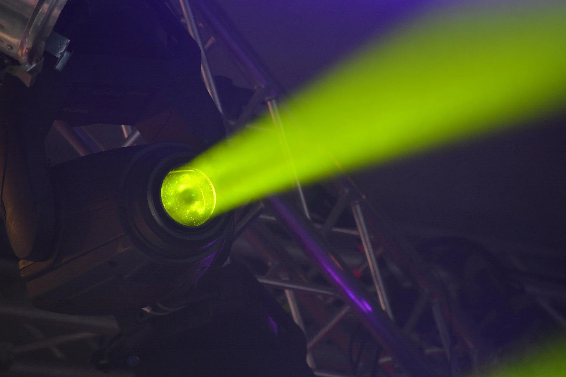 Close-up of a stage lighting fixture projecting a green laser beam into the dark background.