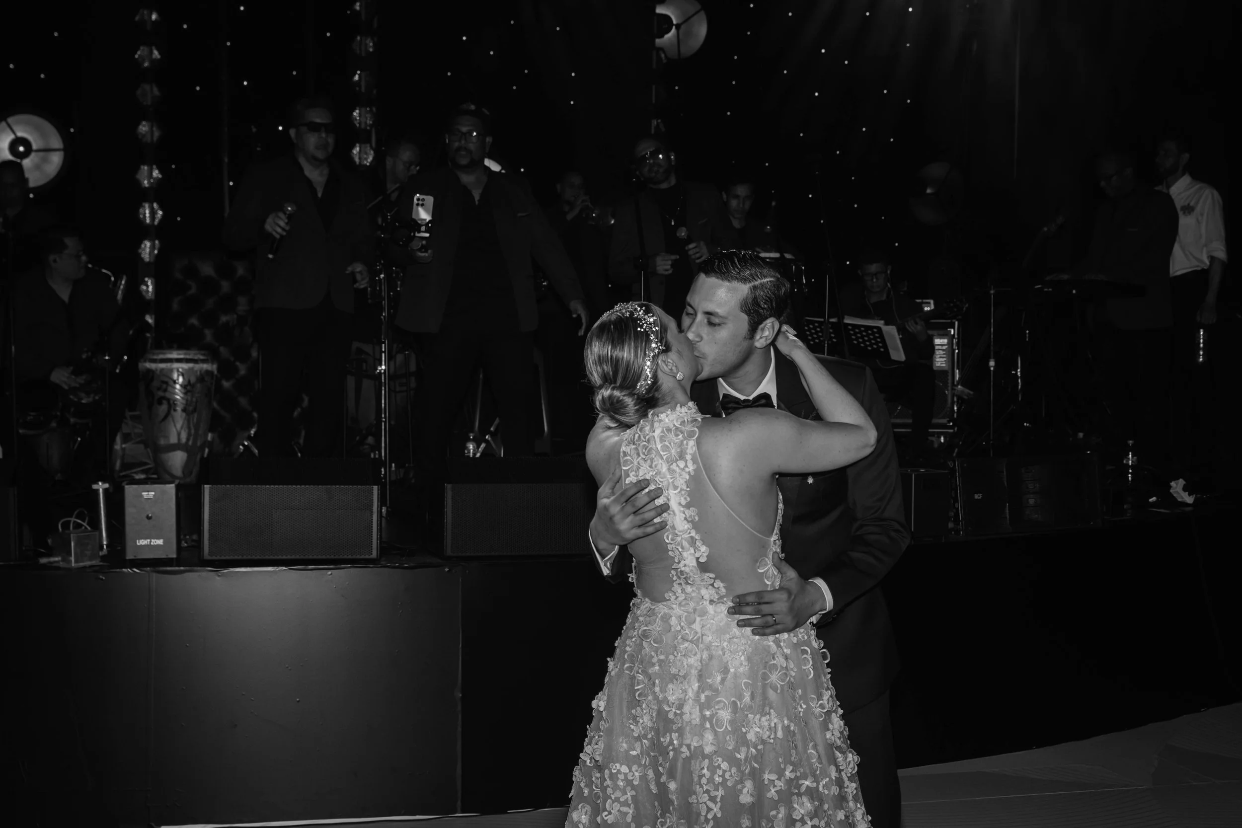 A bride and groom sharing a kiss during their wedding dance, with a band playing in the background.