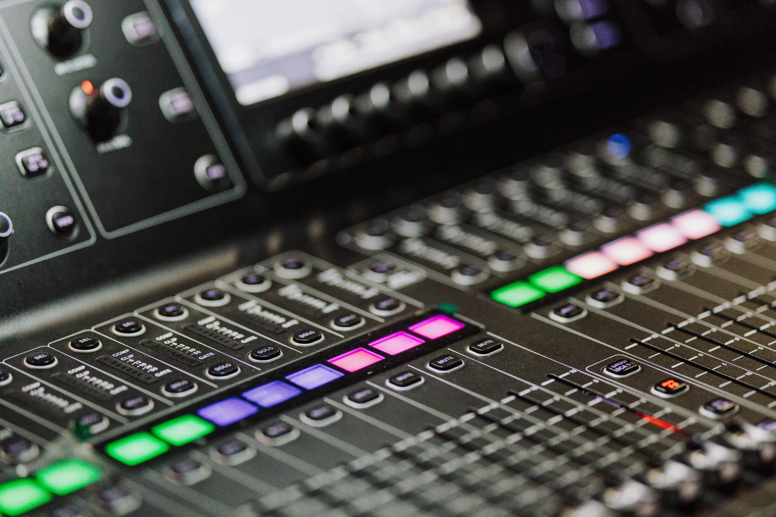 Close-up of a professional audio mixing console with colorful illuminated buttons and faders.