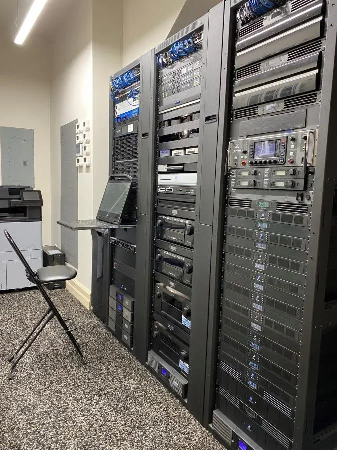 Theater stage decorated with blue curtains, featuring dancers in white costumes, some with bows, performing a ballet or dance routine. Sparkling confetti or snow falling from above, with stage lighting creating a magical atmosphere.