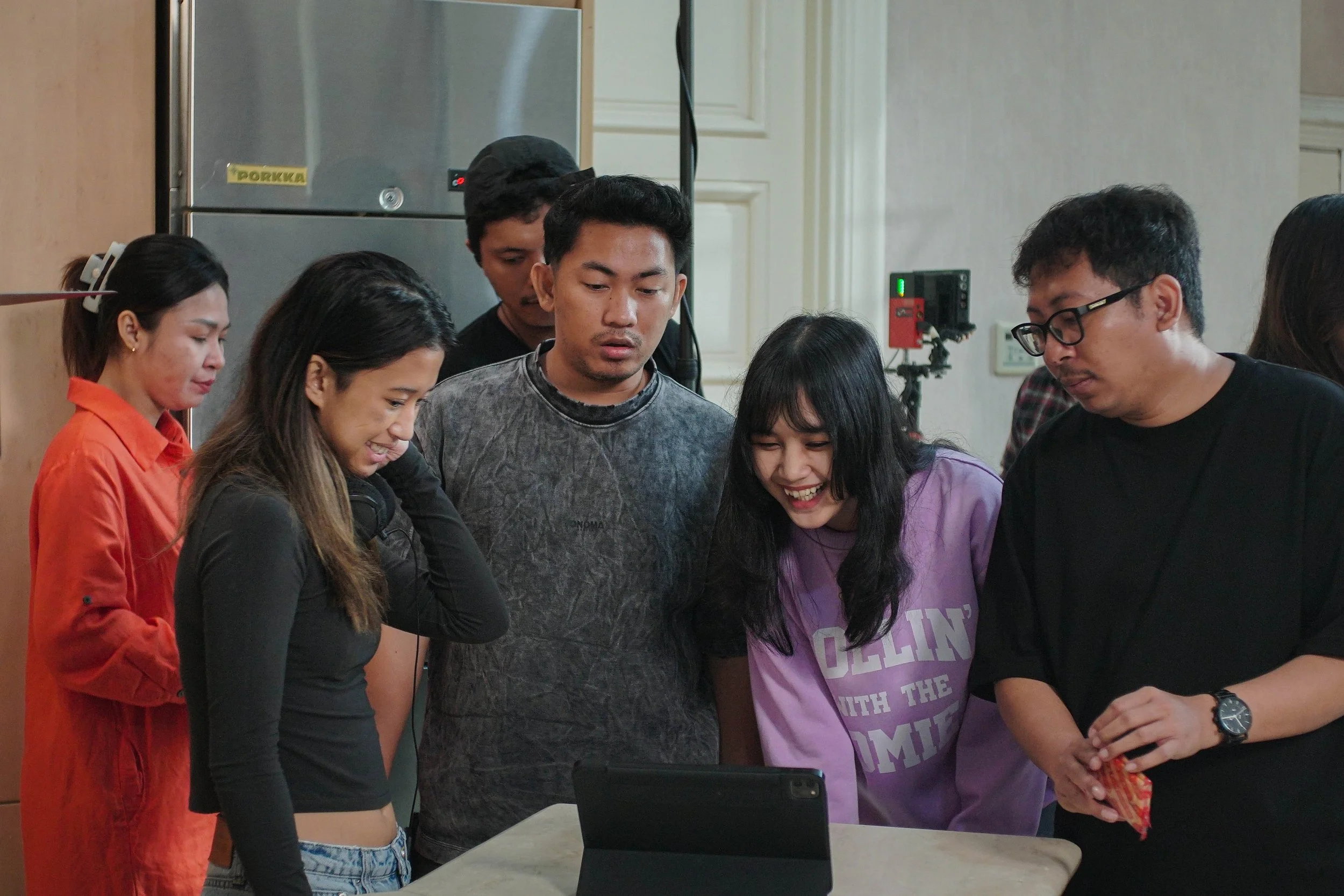A group of people gathered around a tablet, smiling and looking at the screen.