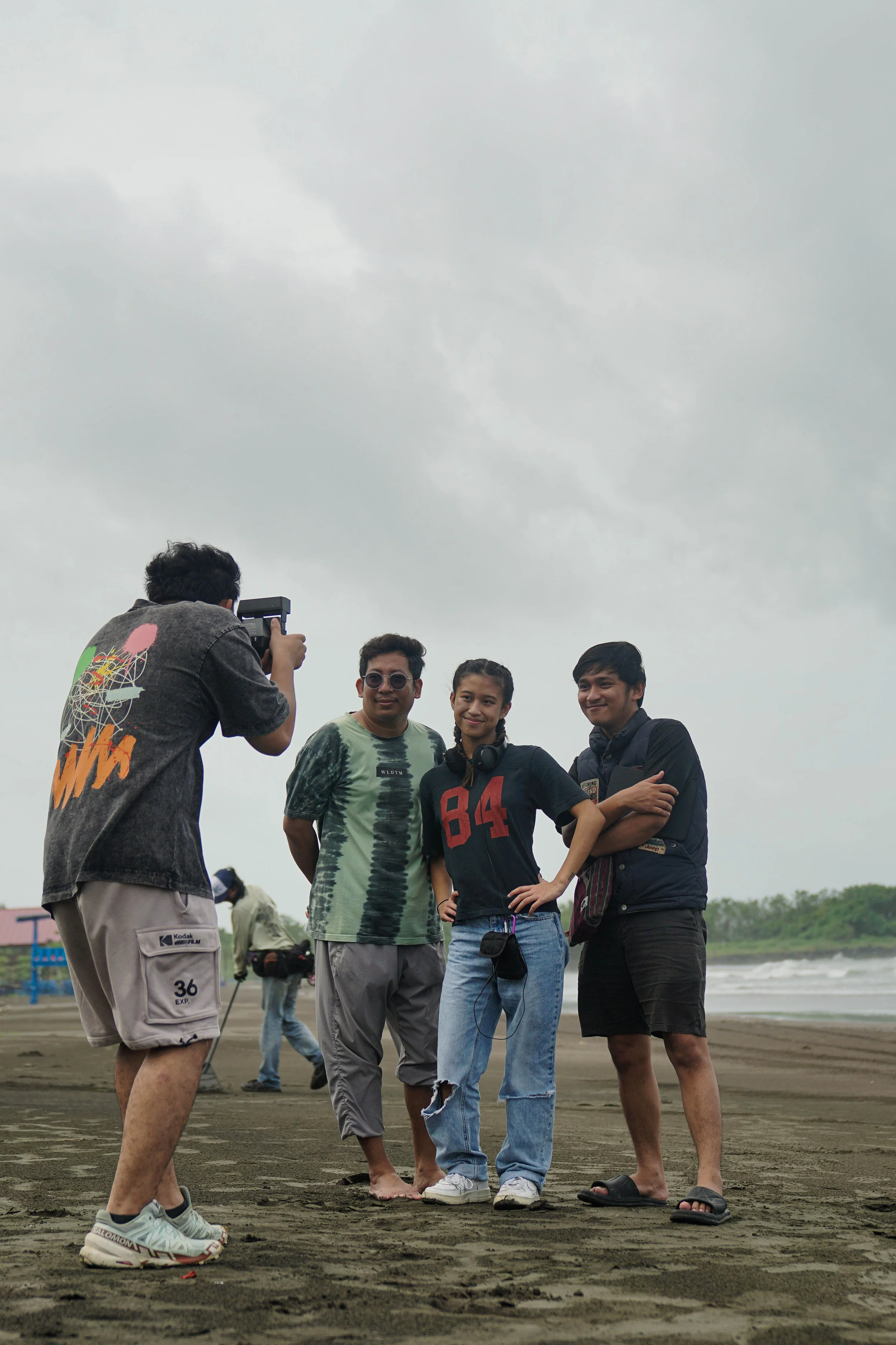 Four friends on the beach taking a group photo with overcast skies in the background.