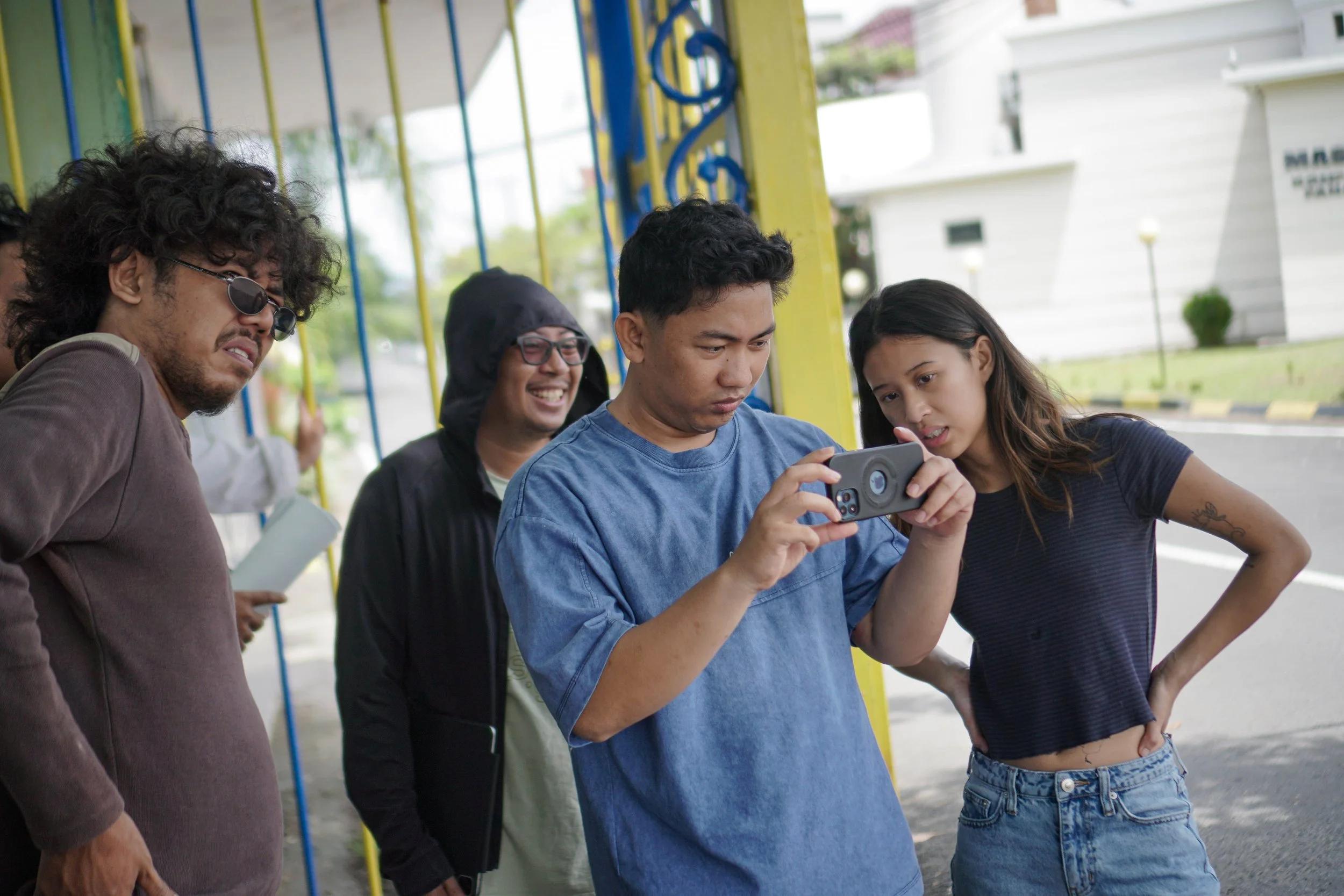Group of young adults standing outside, looking at a phone screen with interest and curiosity.