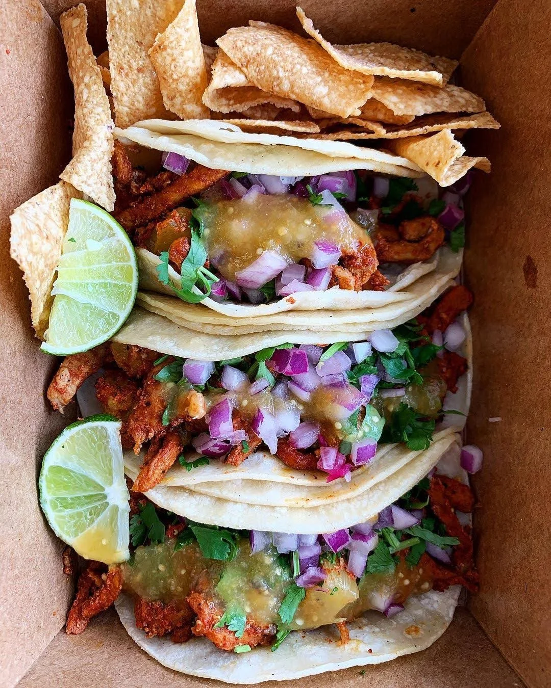 Taco Tour on Lake Street. These street-style tacos are topped with chopped red onions, cilantro, and a green sauce, served with lime wedges and a side of crispy tortilla chips.