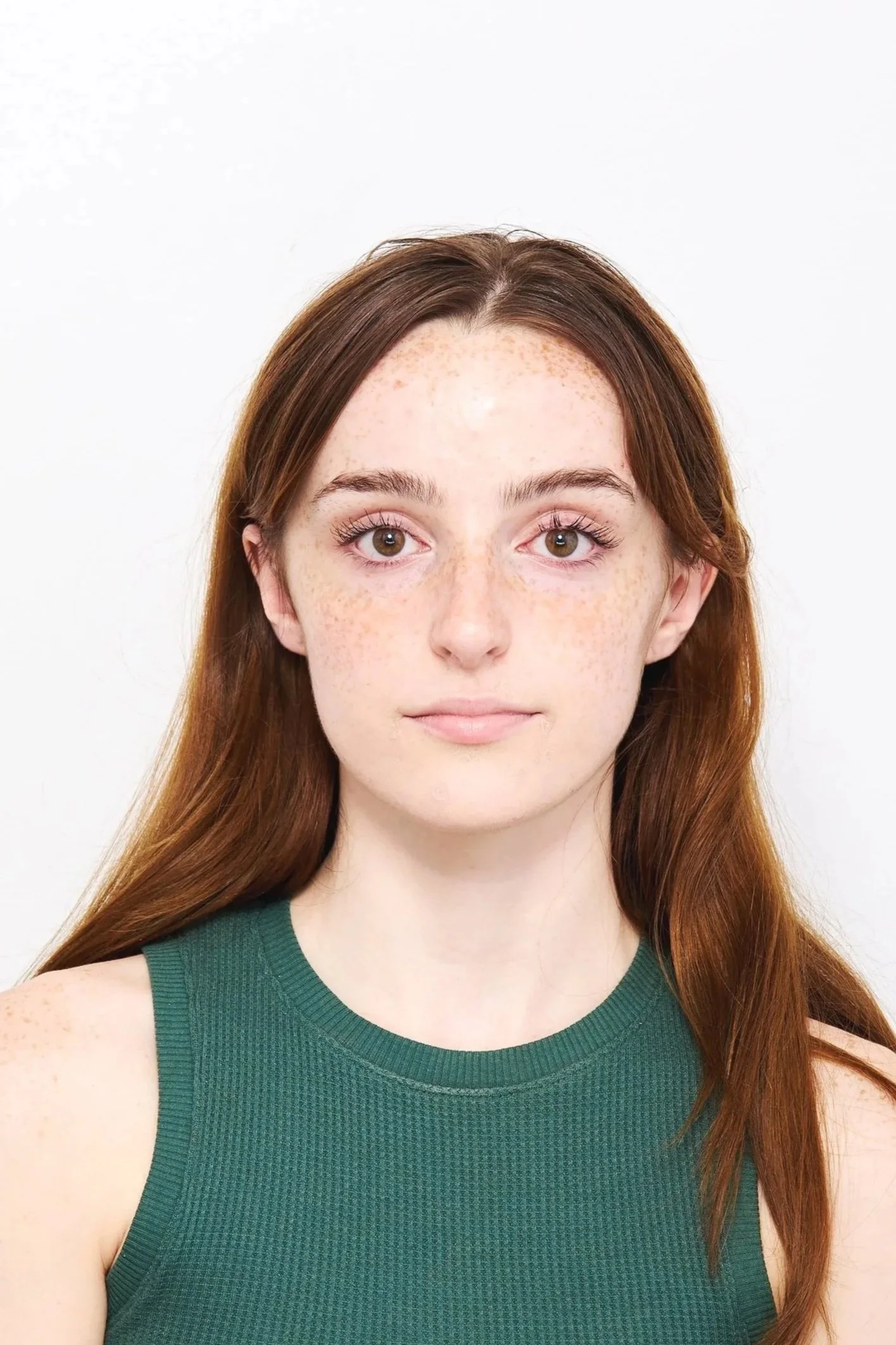 A young woman with long red hair and green eyes, wearing a green sleeveless top, looking directly at the camera against a plain white background. Passport photo.
