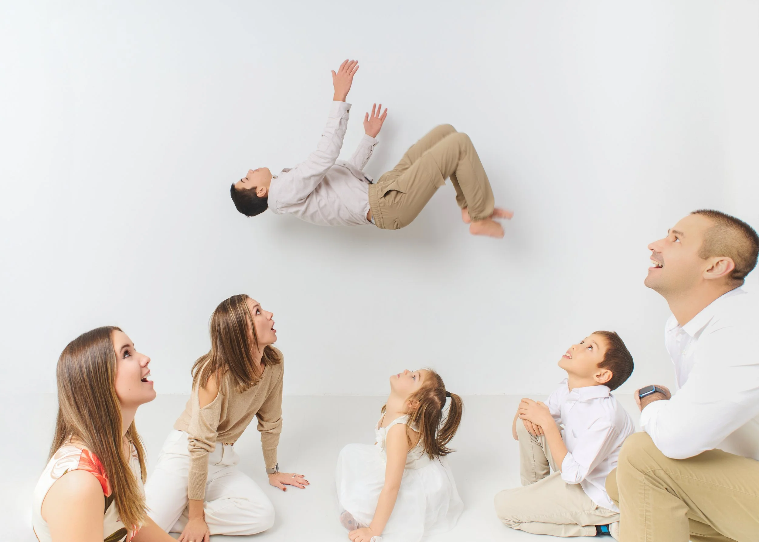 Family of four with three children and one adult looking up at a boy falling backwards against a plain white background
