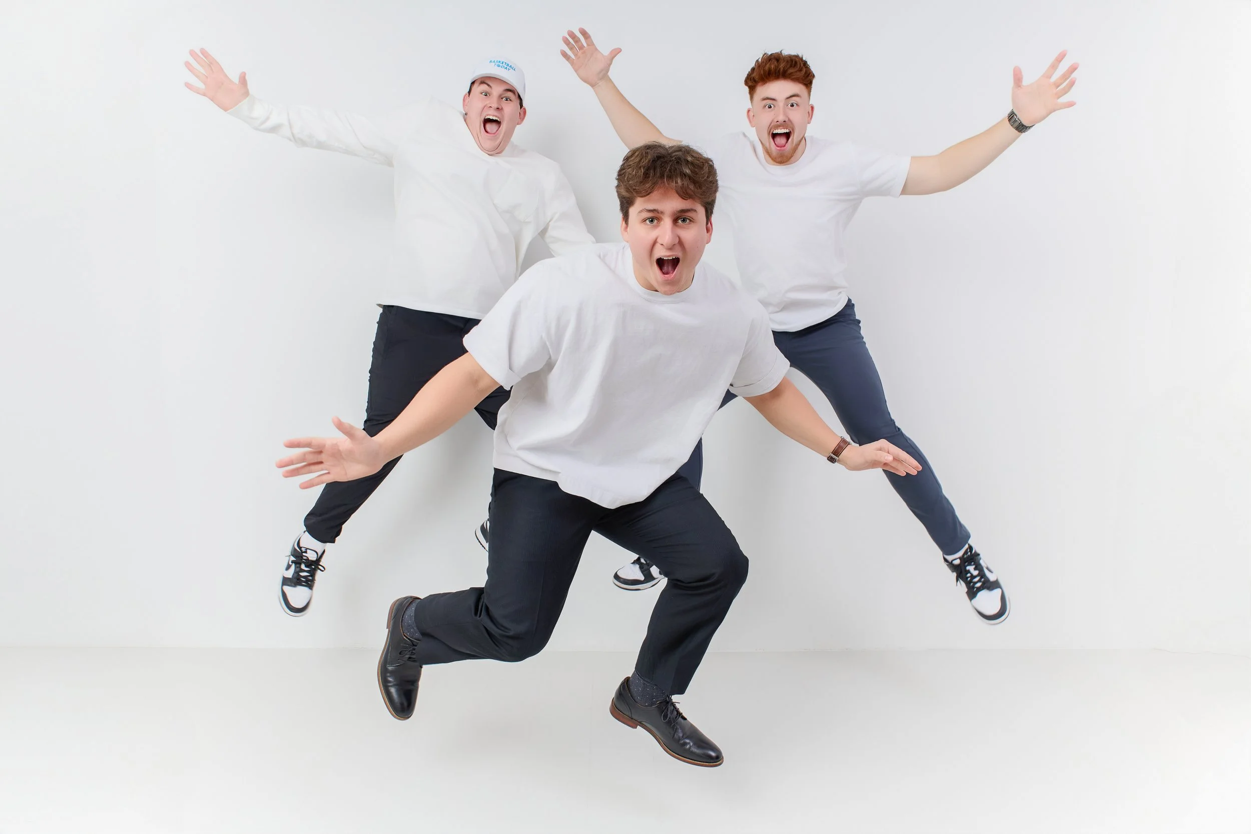 Three young men jumping and posing expressive in front of a plain white wall.