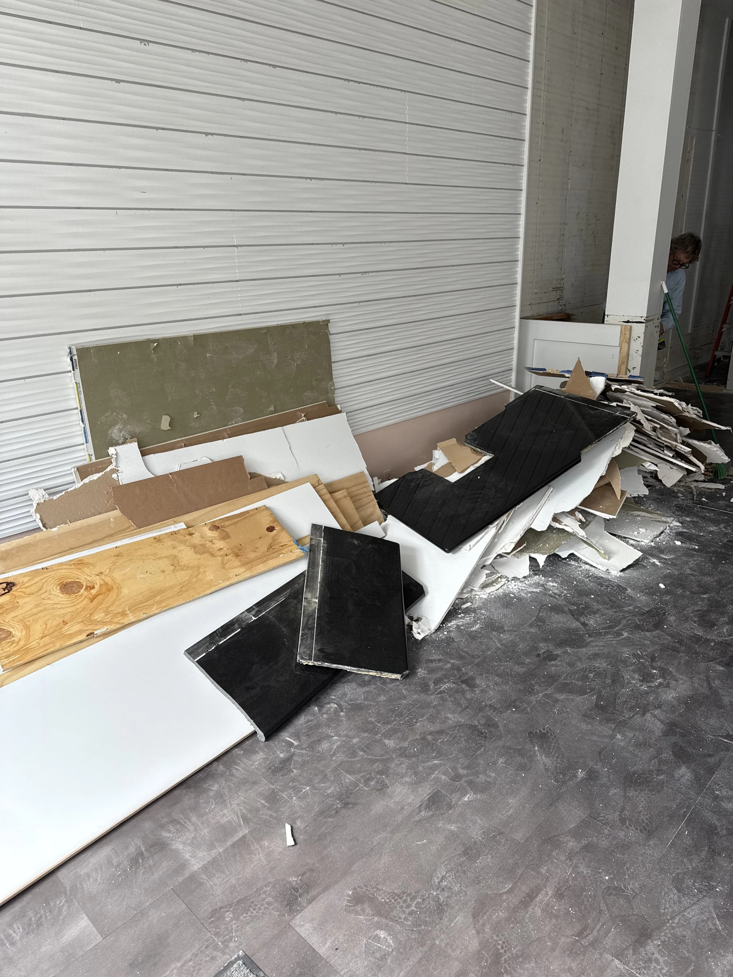 Pile of broken drywall, wood, and construction debris on the floor in front of a partially finished wall.