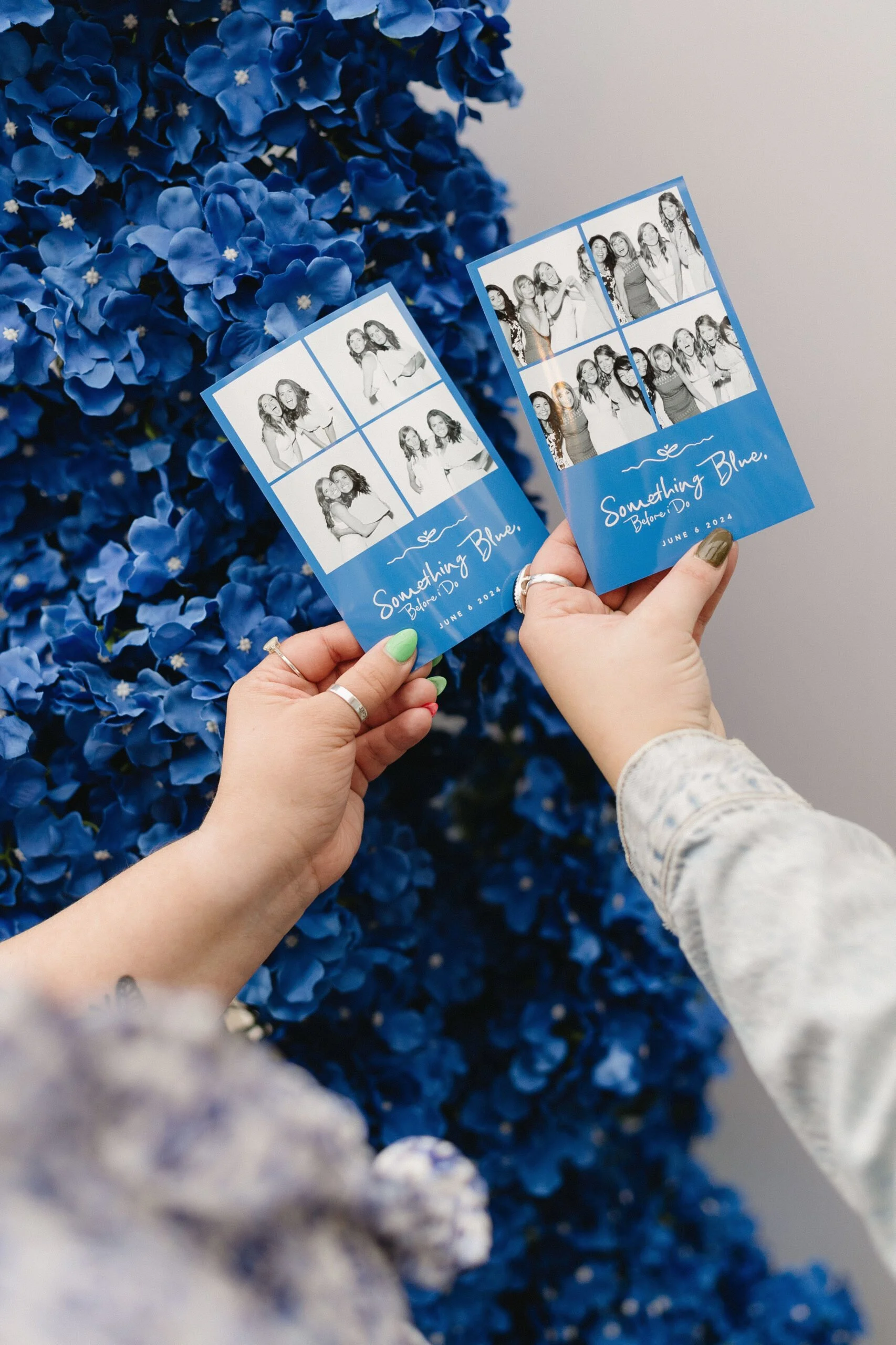 Two people holding photo booth prints with four photos each, featuring a group of women, against a backdrop of blue hydrangea flowers. The prints have the text 'Something Blue, Before I Do' and the date June 6, 2024.