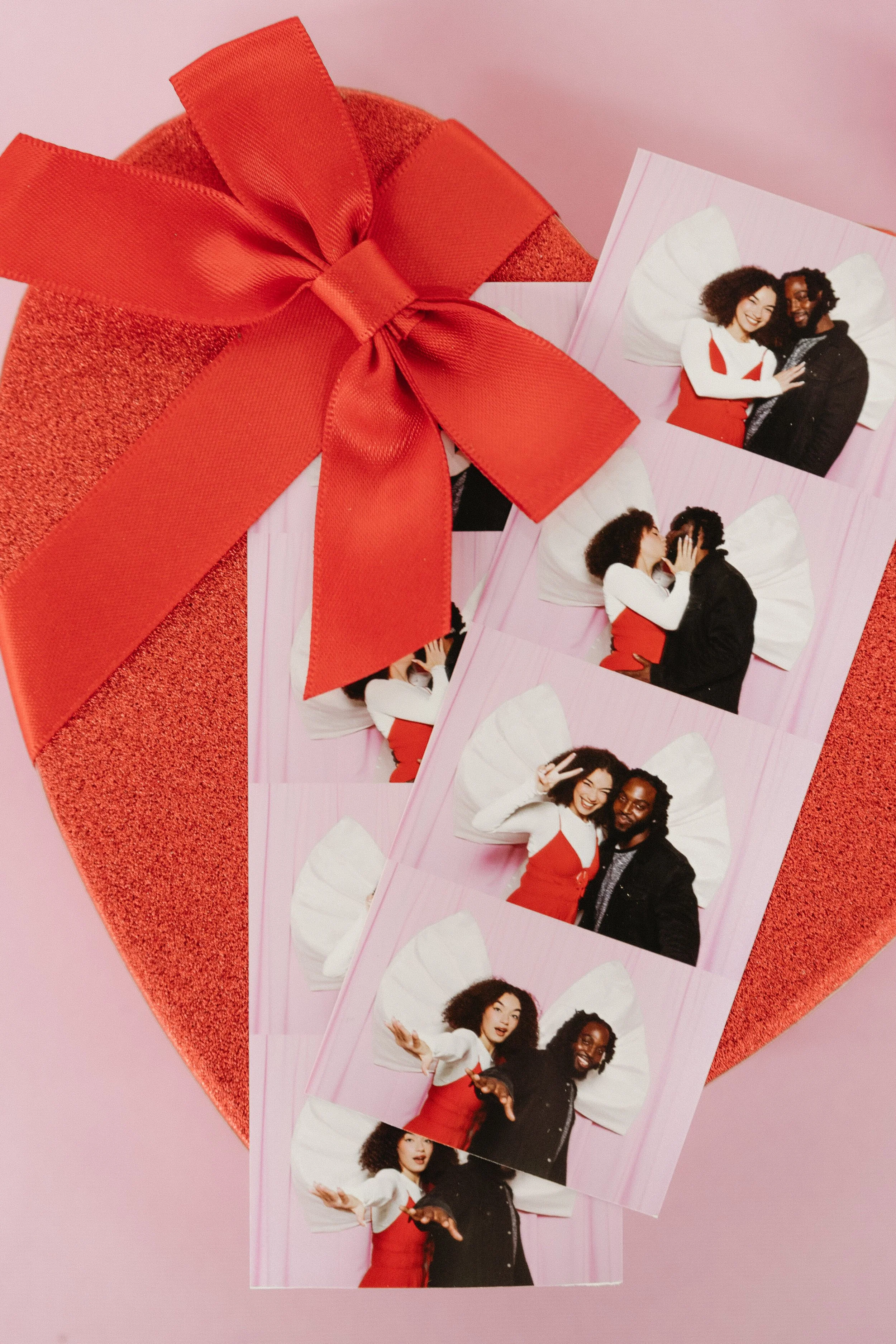 Photo booth strip with four pictures of a woman and a man with angel wings, with a large red ribboned gift box.