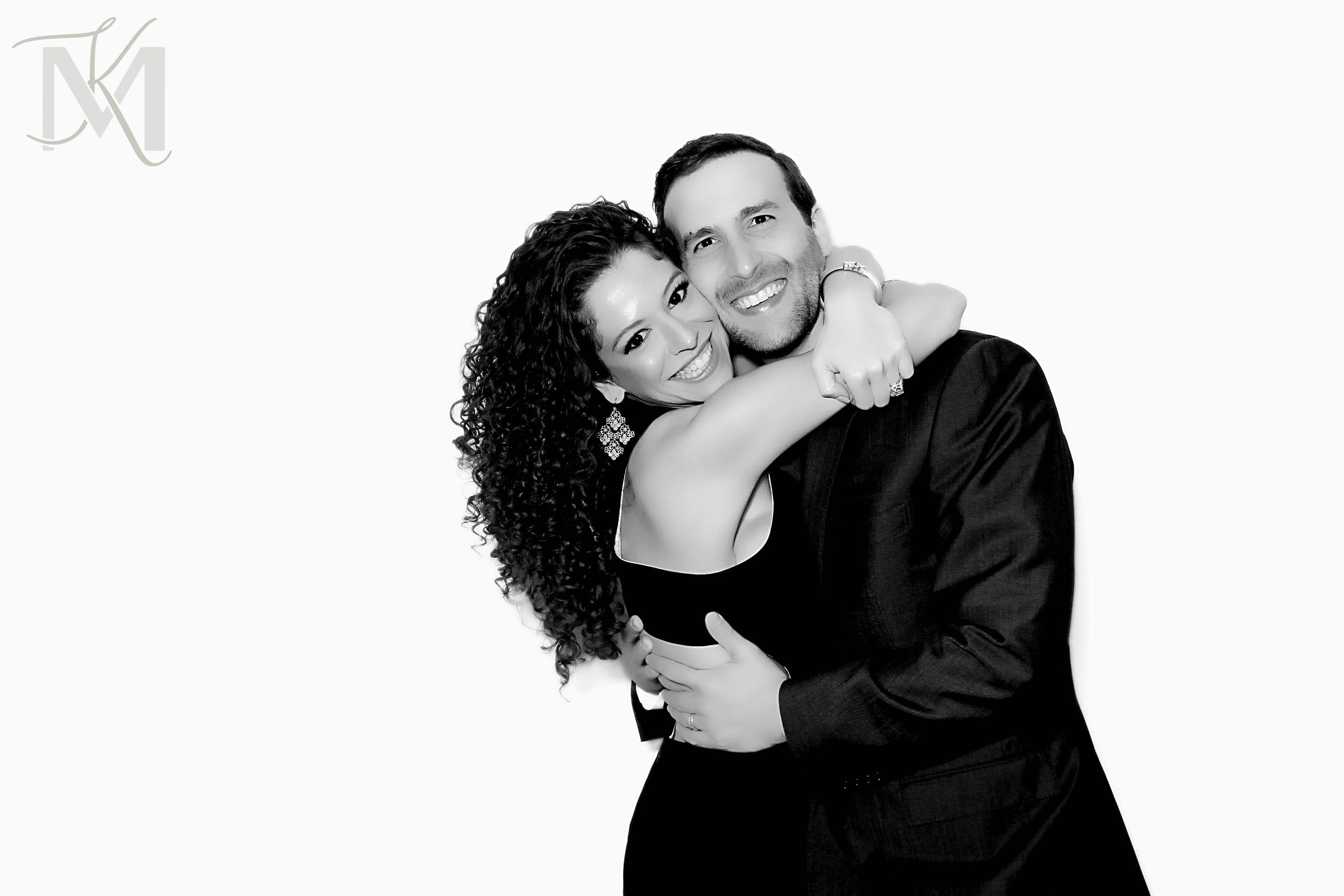 A happy couple, an African American woman with curly hair and a Caucasian man with short dark hair, embracing each other and smiling at the camera.