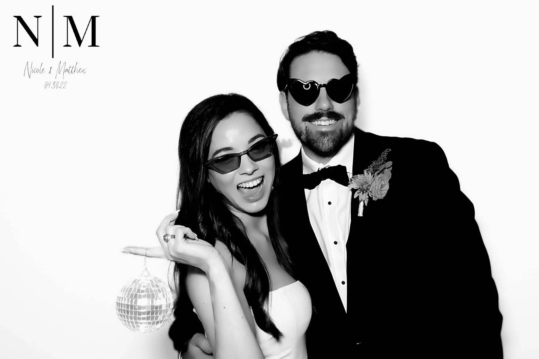 A black and white photo of a happy couple dressed formally, both wearing sunglasses, with the woman holding a small disco ball and the man with a boutonniere on his tuxedo. The top left corner has text reading 'N | M | Nicole & Matthew 04.30.22.'