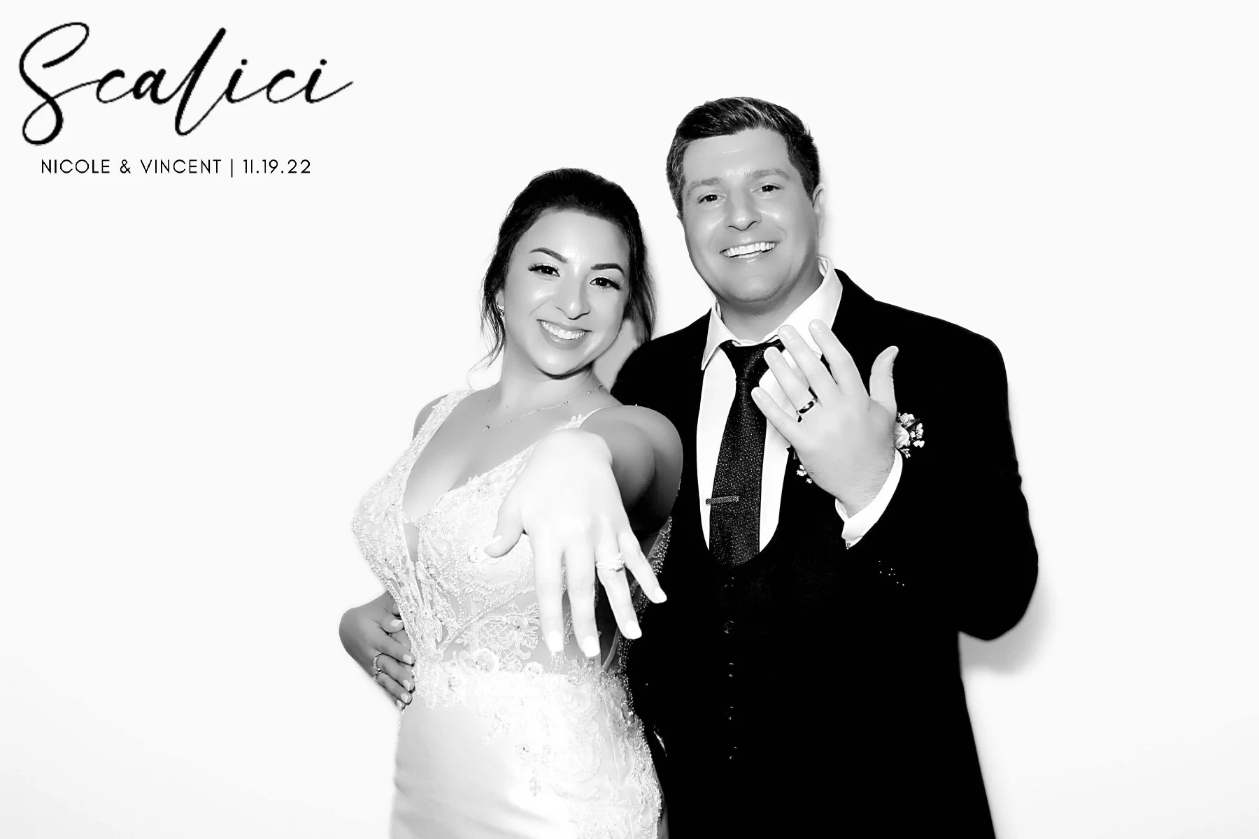Black and white photo of a smiling couple showing their wedding rings, with text indicating their wedding date and names, in front of a plain background.
