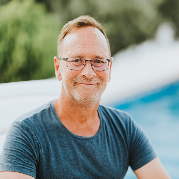 A middle-aged man with glasses and a light beard smiling outdoors, wearing a dark blue t-shirt.