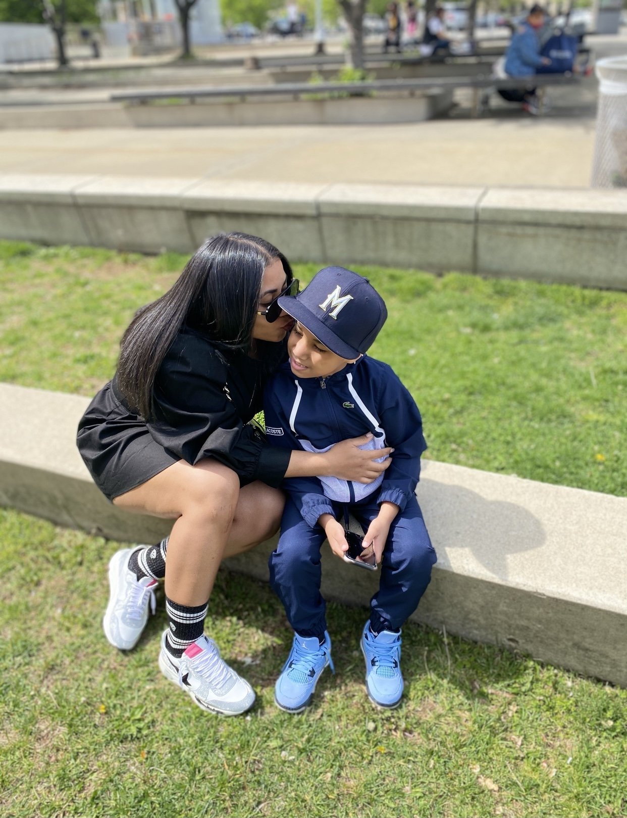 Mother kissing her young son on the cheek while sitting outdoors, symbolizing love, joy, and motherhood.