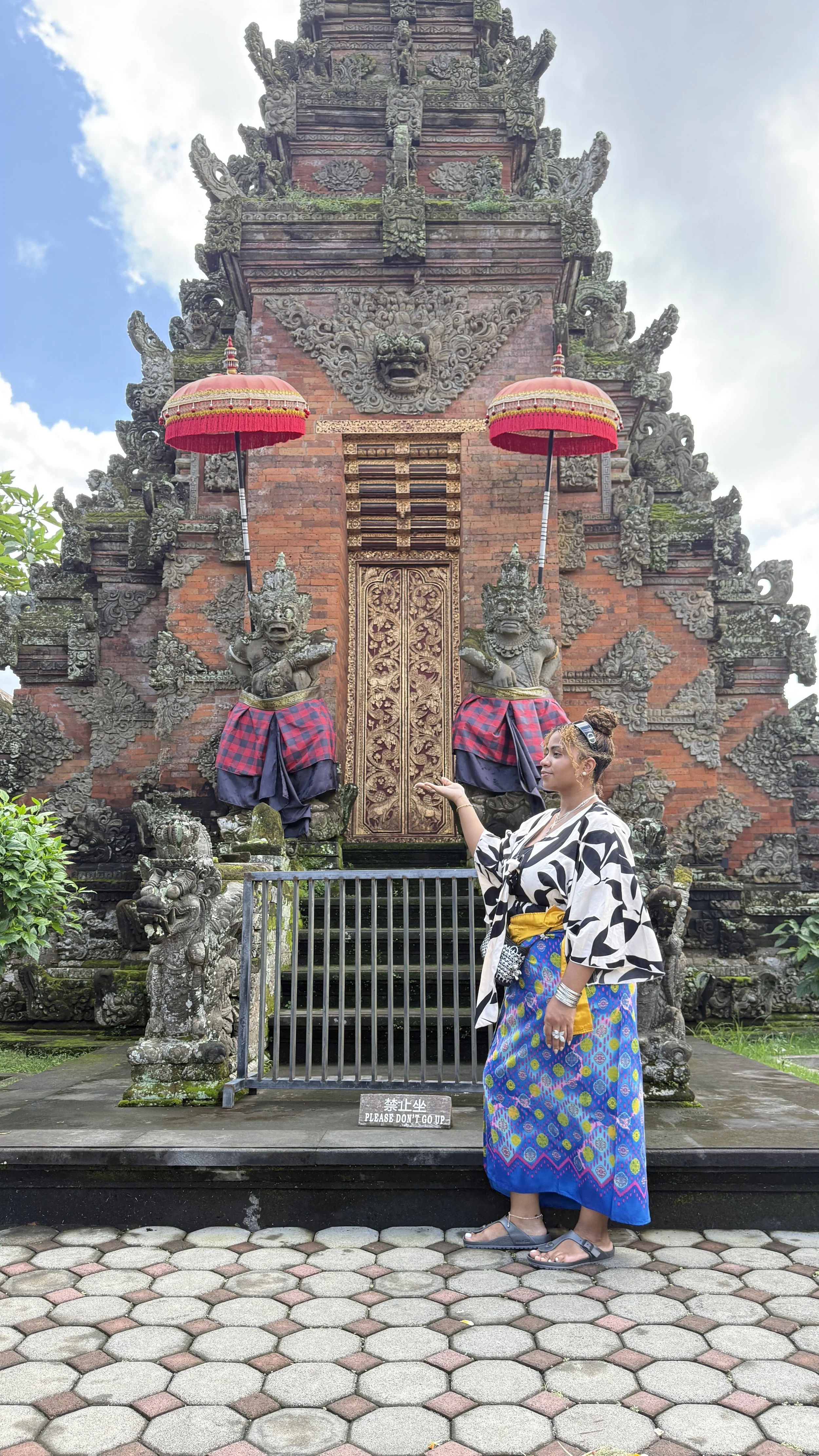 Woman standing in front of a traditional Balinese temple in colorful sarong, representing travel, culture, and exploration.
