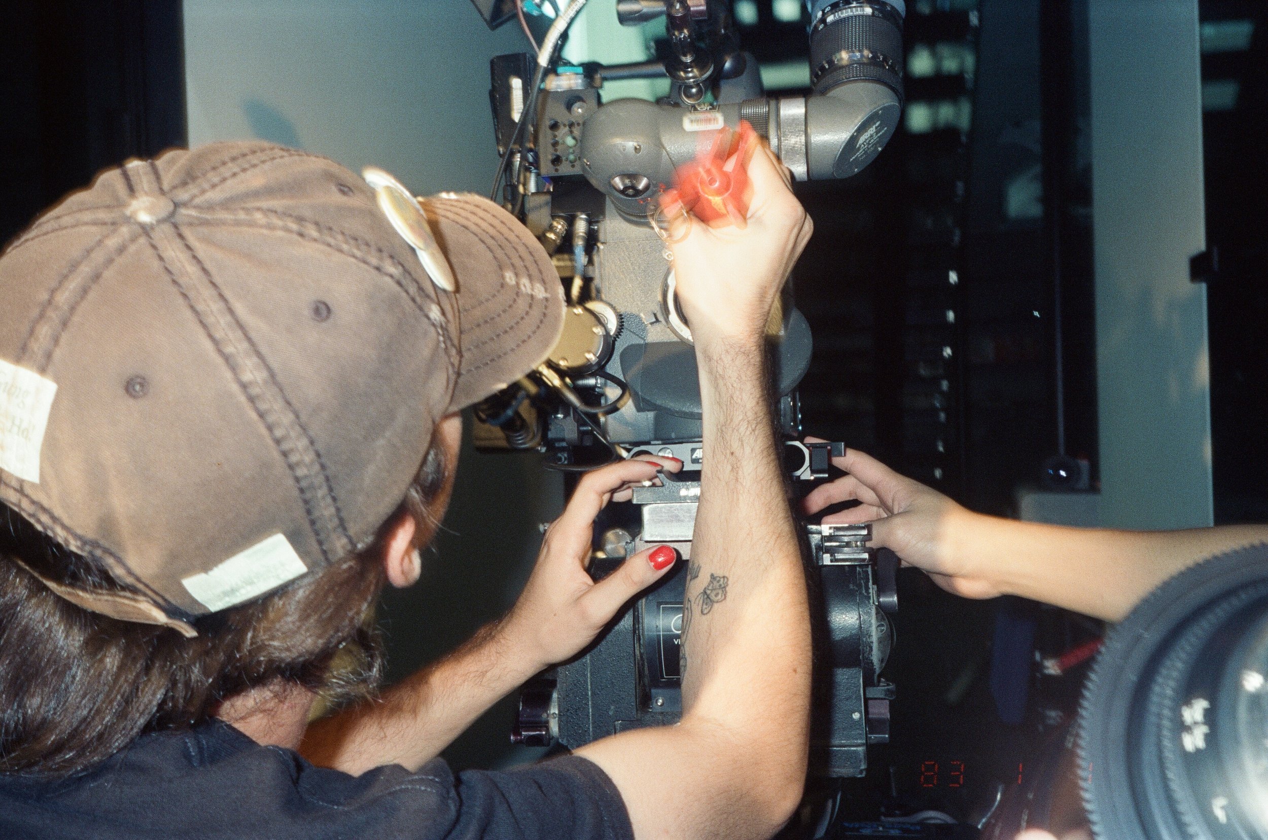Two crew members adjust the camera together, one with red nail polish.