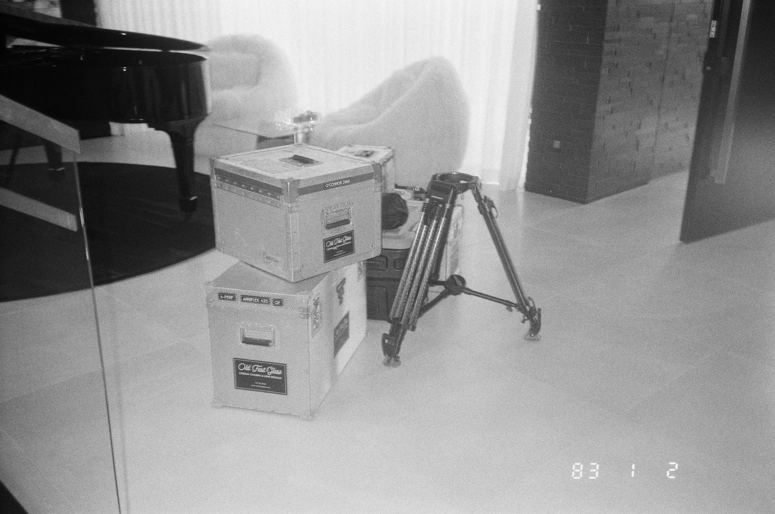 Two Old Fast Glass flight cases stacked beside a tripod and a grand piano.