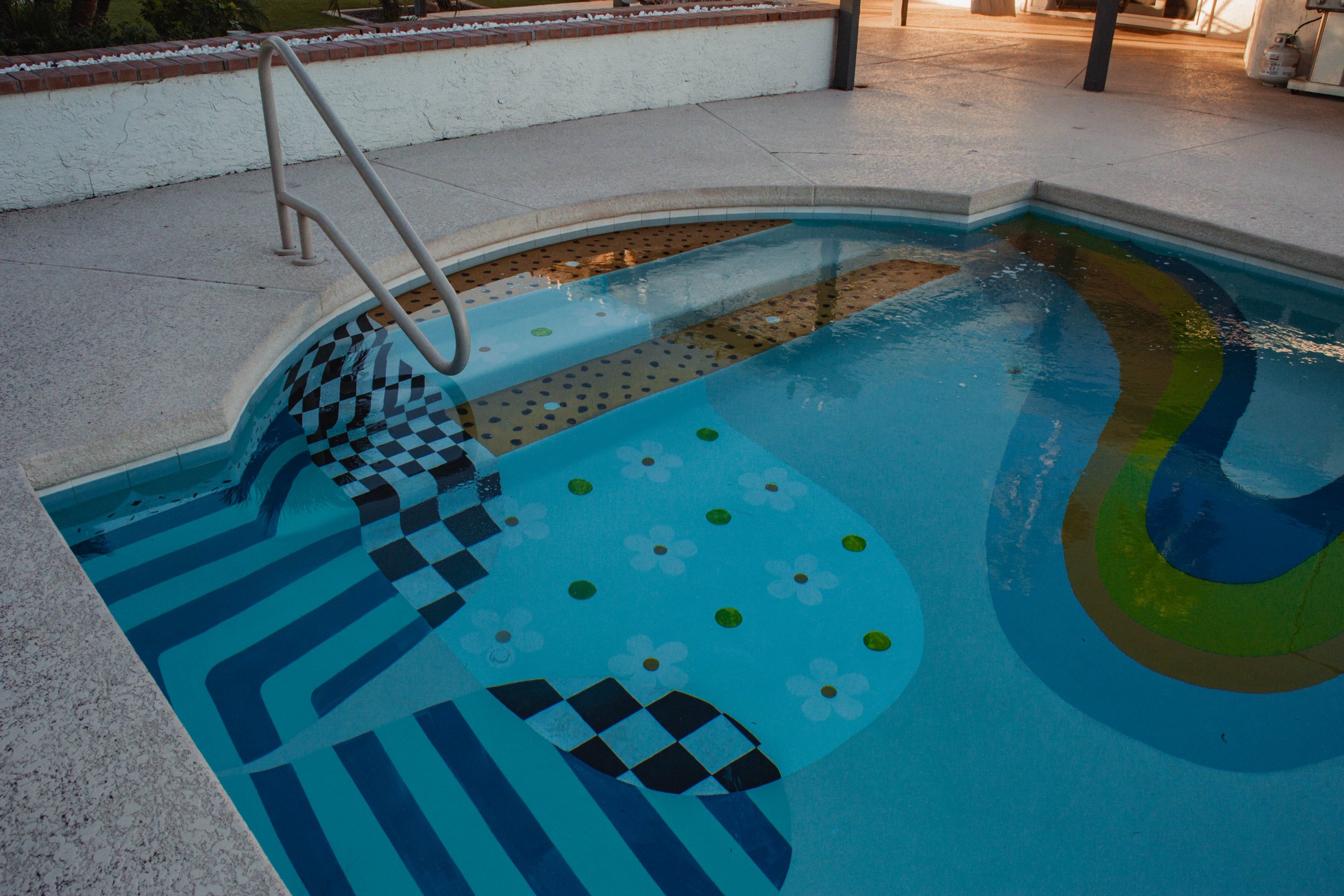 Decorative swimming pool with colorful patterns and tiles, metal handrails at the entrance, and an outdoor setting with concrete and brick surroundings.