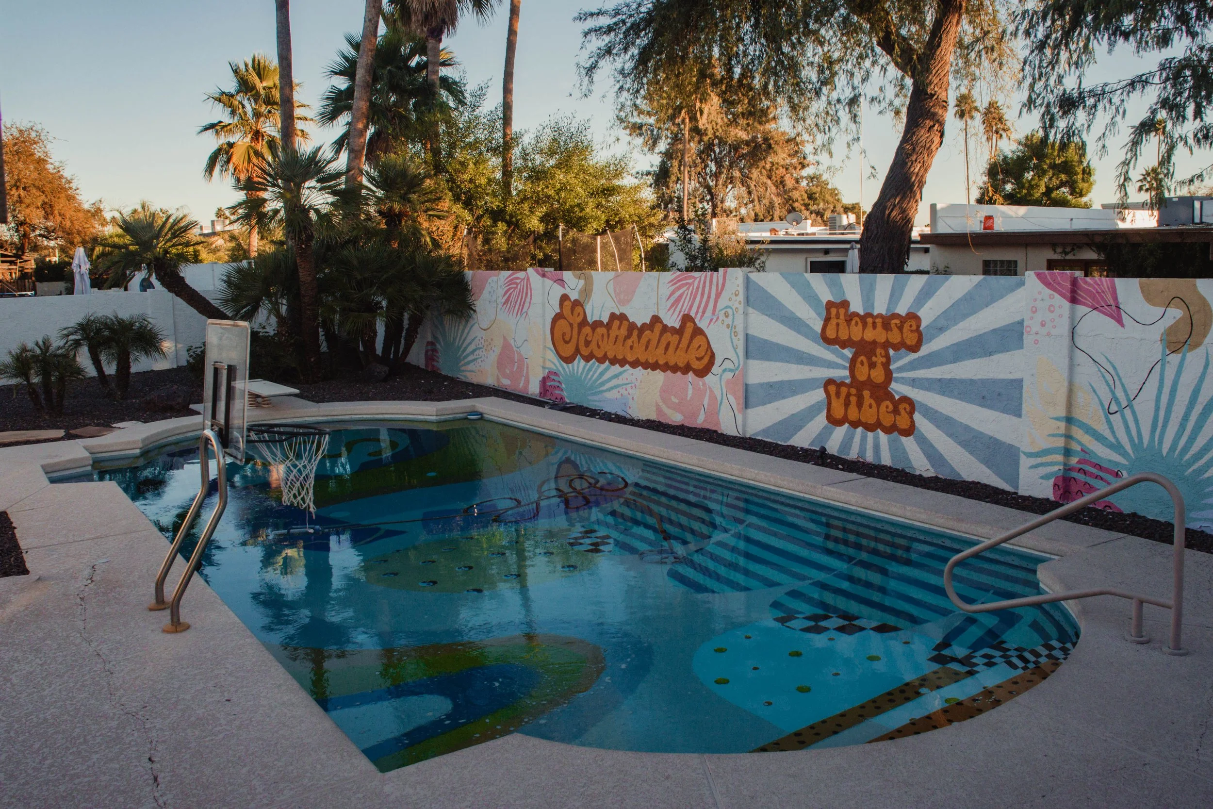 A backyard pool with a colorful mural wall in the background, featuring the words 'Jungalow' and 'House of Vibes'.