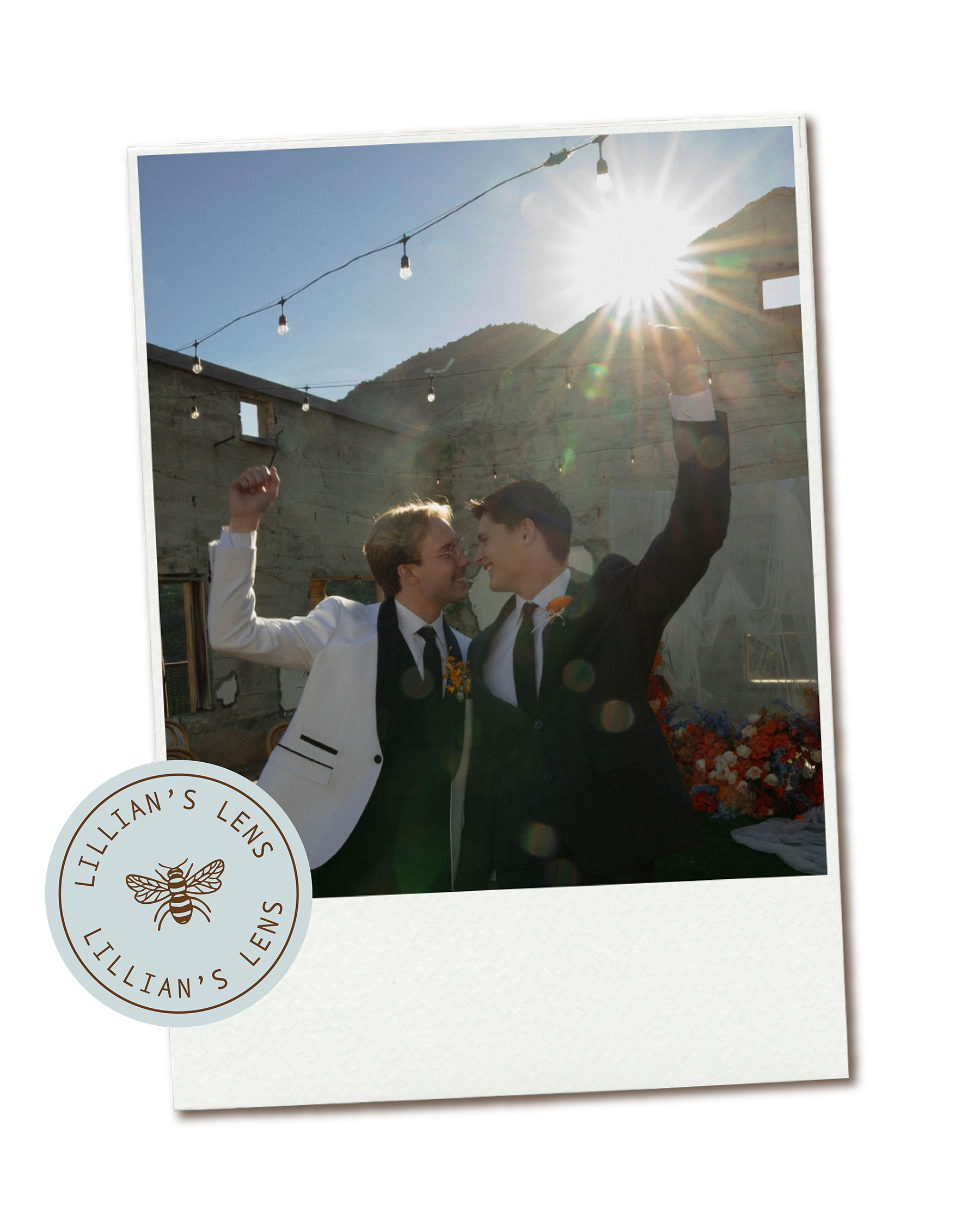 Two women in wedding attire celebrating, holding hands and looking at each other outdoors with sunlight shining over them and string lights above.