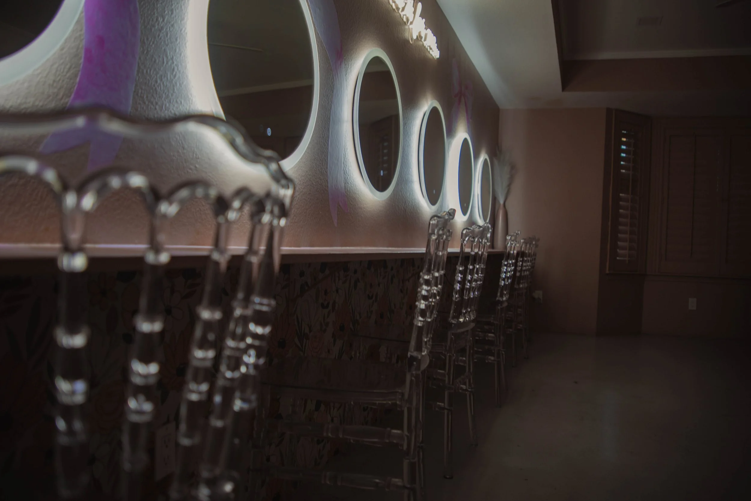 A bar counter with illuminated circular mirrors and transparent acrylic chairs in a dimly lit room.