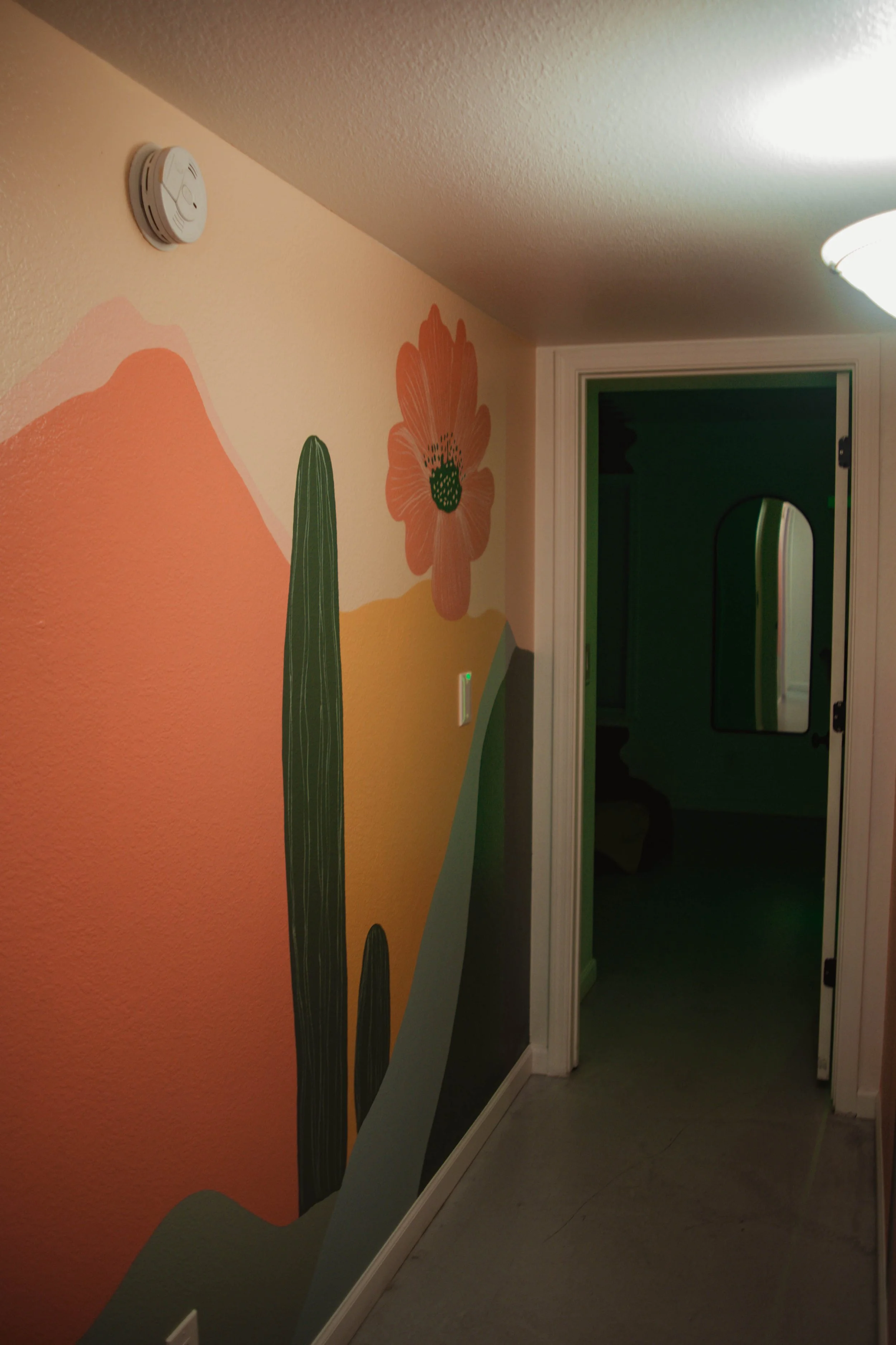 Colorful desert scene mural including a cactus, a large flower, and mountains painted on a wall in a hallway.