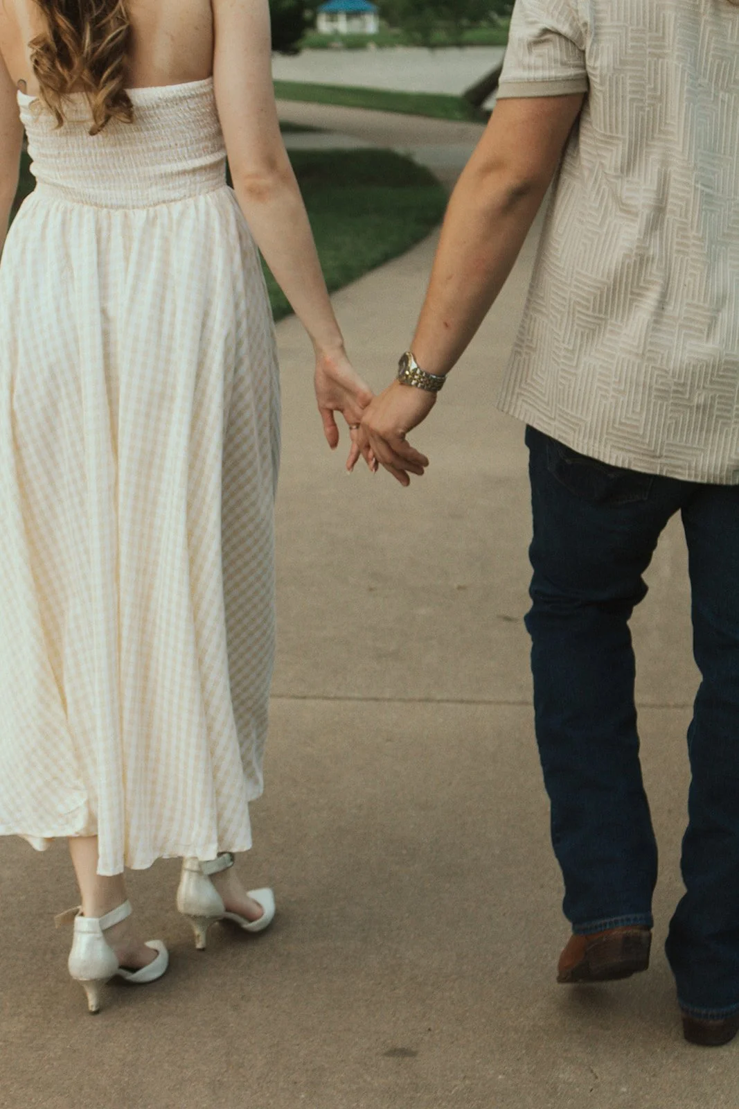Close up of a couple holding hands walking down a sidewalk in the park