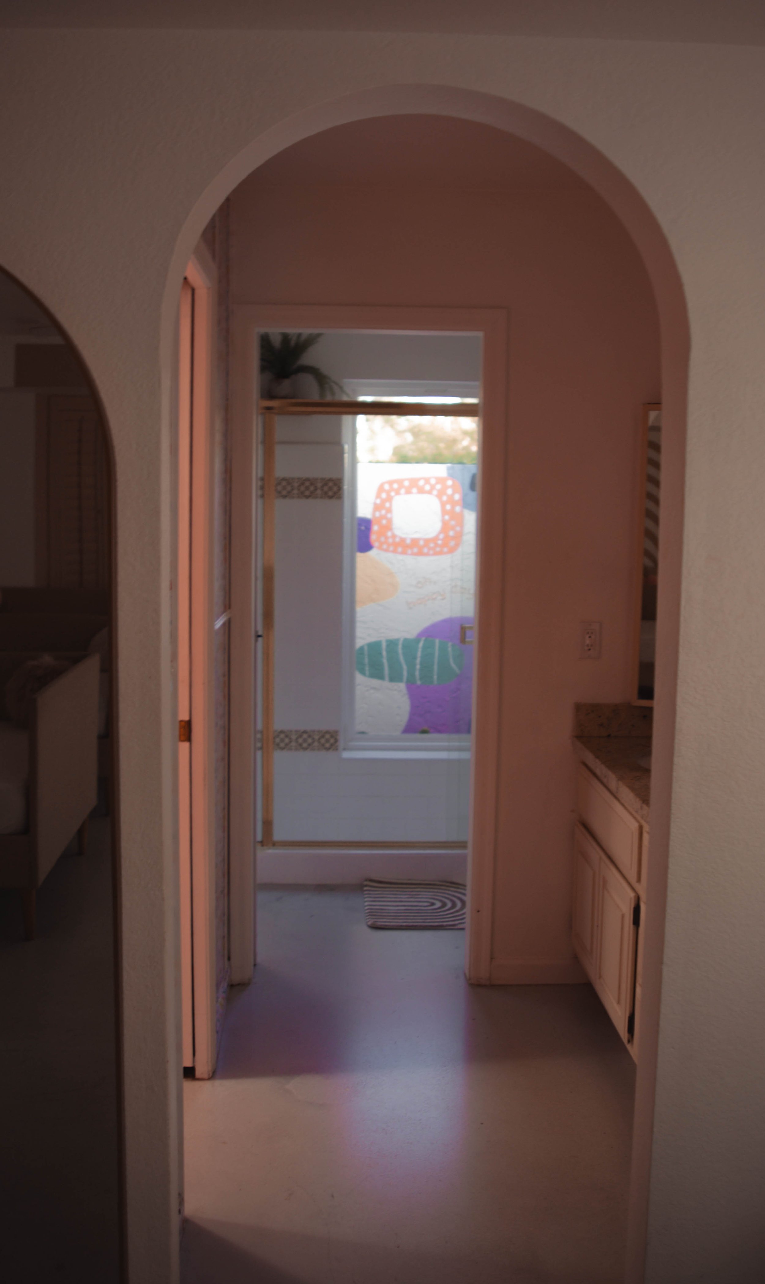 View through a doorway into a bathroom with a window featuring colorful abstract stained glass.