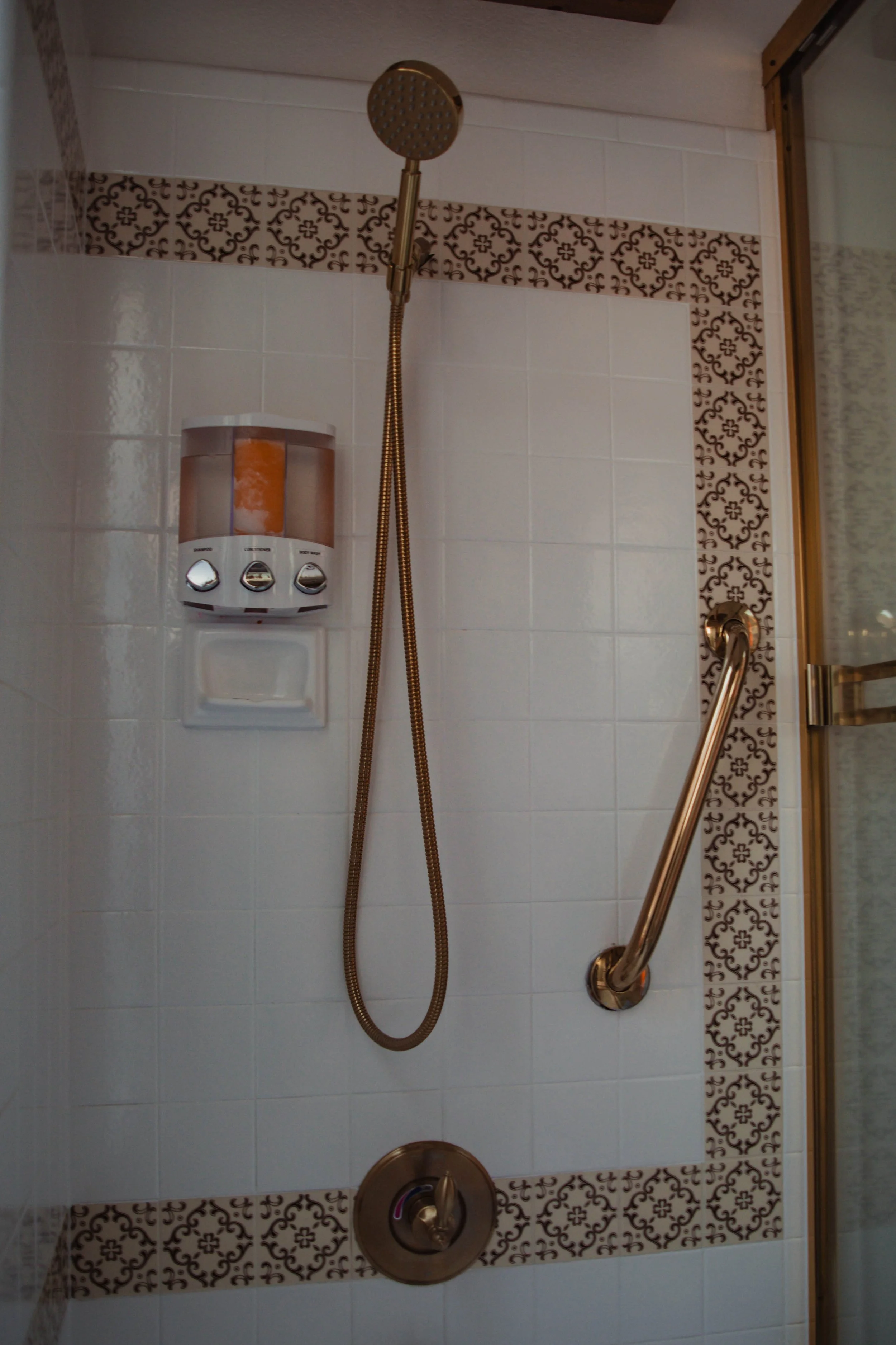 Shower area with a handheld showerhead, a soap dispenser, and a grab bar on the wall.